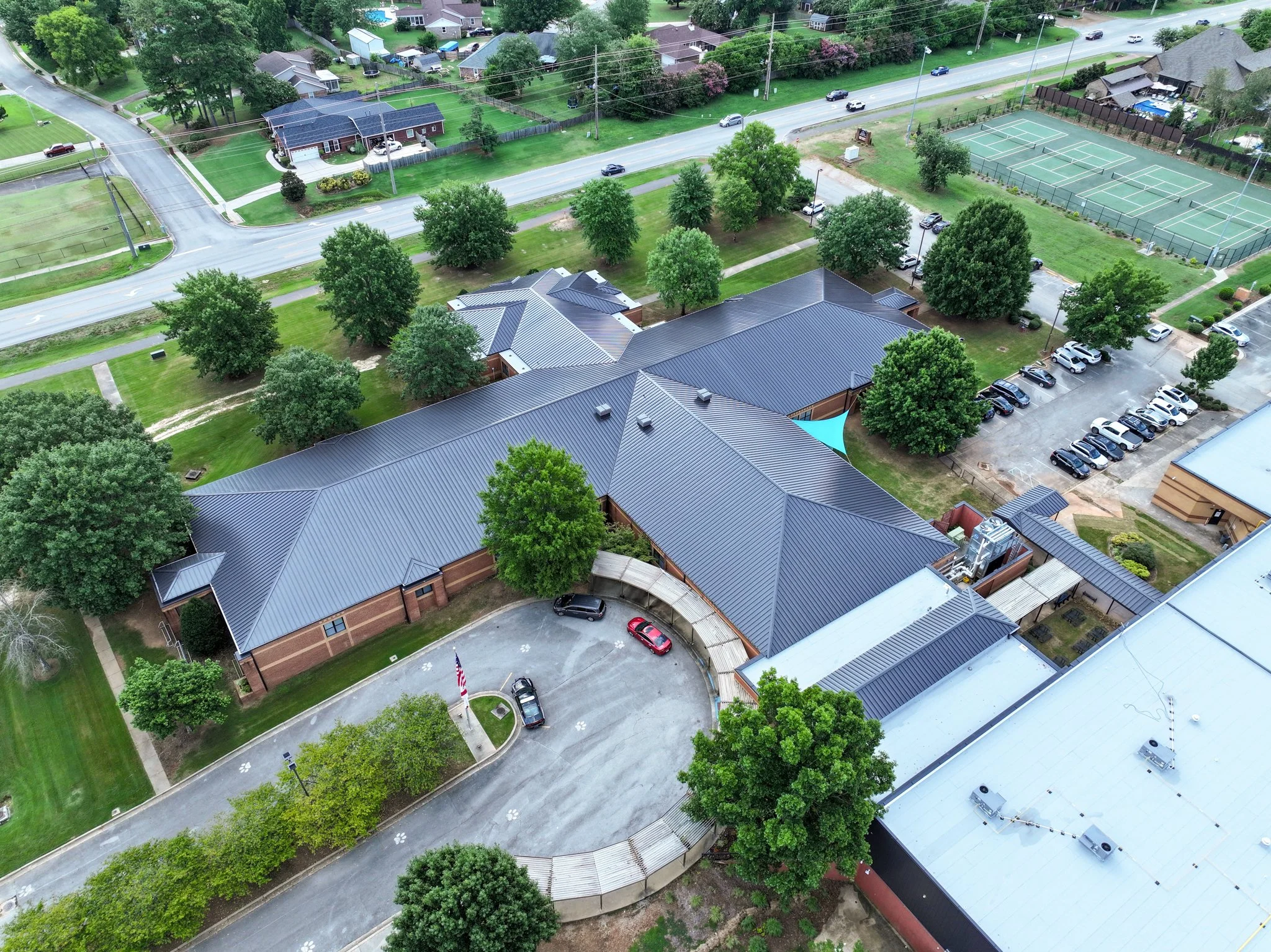 An aerial view of a Discovery Middle School, trees, a tennis court, parking lots, and a road with cars.
