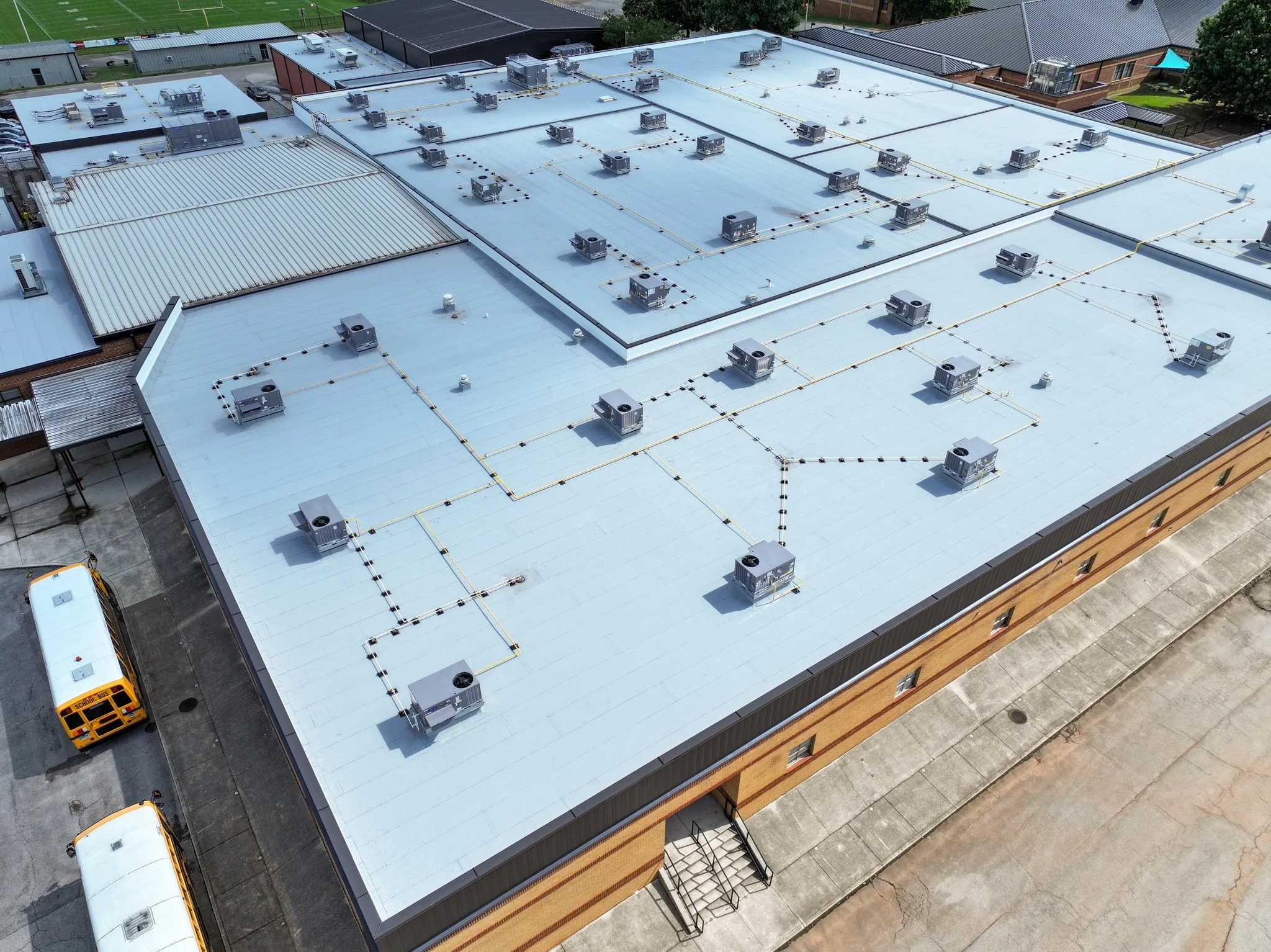 Aerial view of Discovery Middle School rooftop with multiple HVAC units and piping installations, with surrounding structures and a school bus parked nearby. Built by P&C Construction.