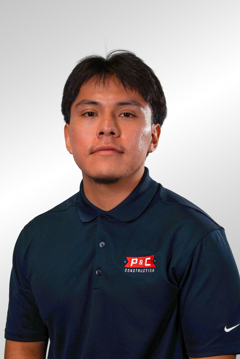 A young man with black hair wearing a black shirt with a red and white logo that reads "P&C Construction" on the chest, standing against a dark background.