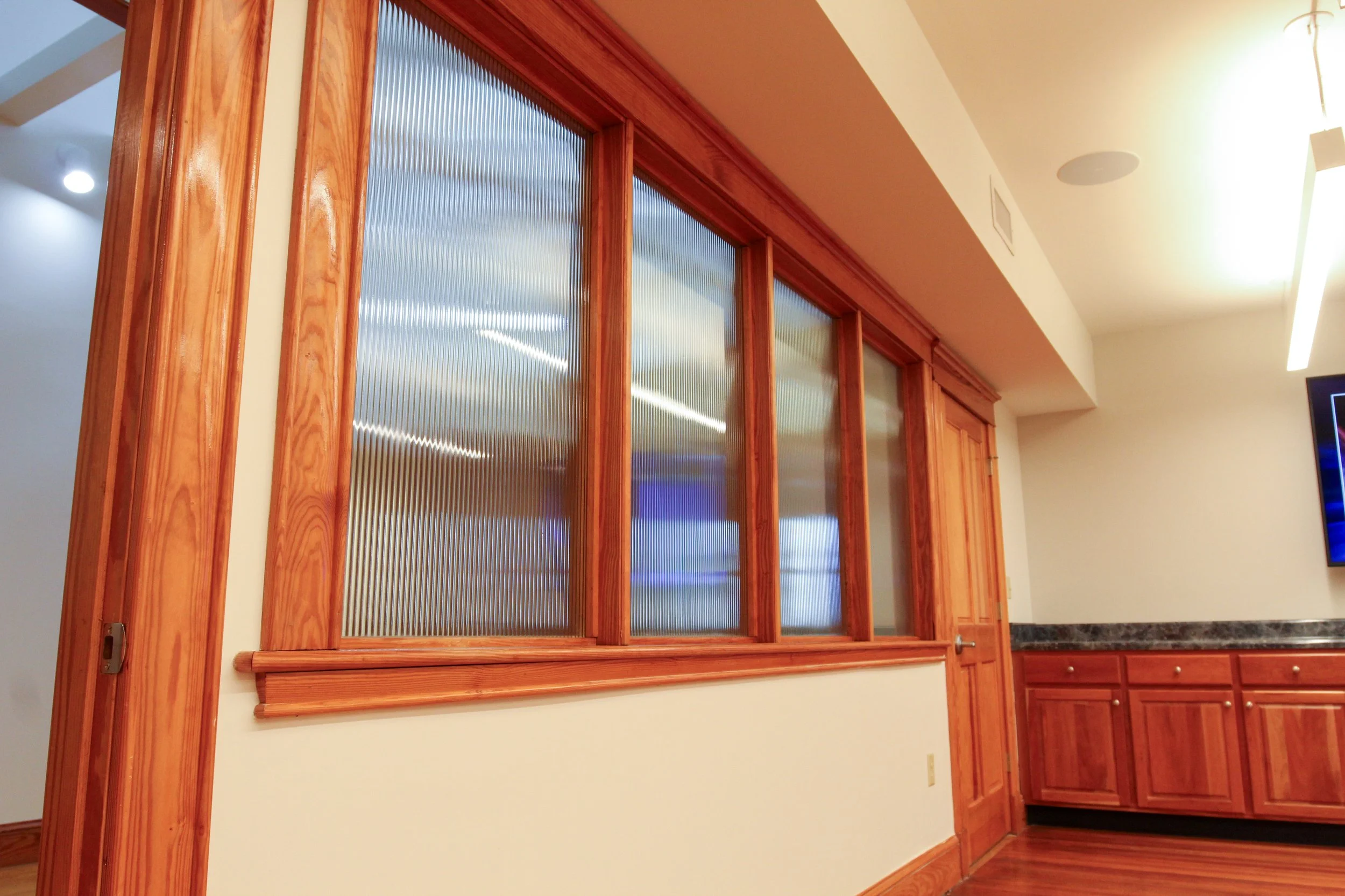 Wooden-framed glass partition with ribbed glass, set in an interior space with wood trim, cabinetry, and a television screen.