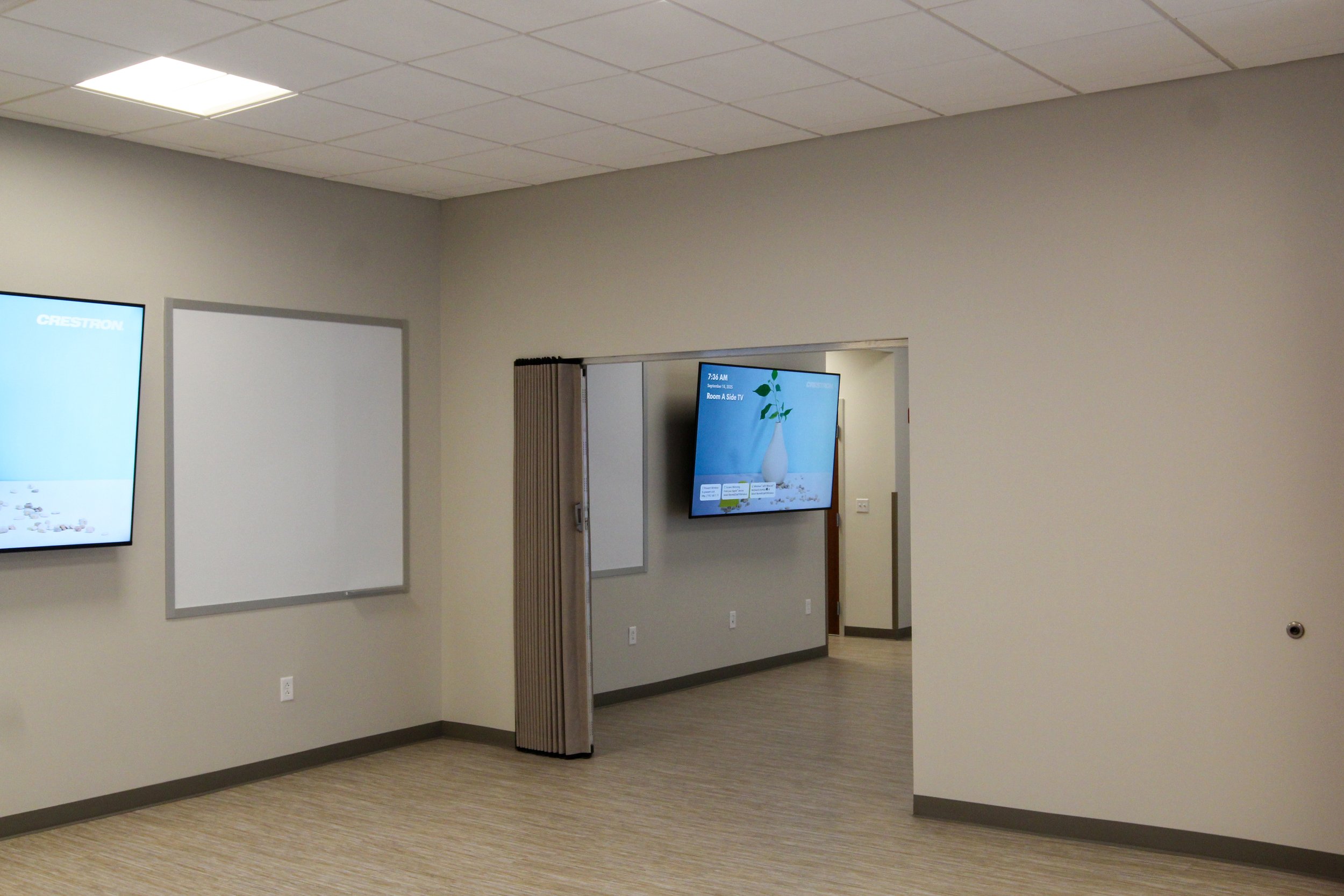 Empty room with wall-mounted screens, plain beige walls, and a partially open folding door.