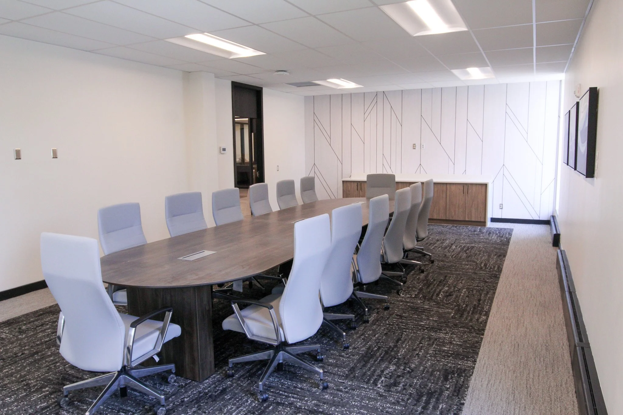 An empty conference room of Simmons Bank in Athens, TN with a long wooden table surrounded by white chairs, a wall with a geometric pattern, and a flat-screen TV mounted on the wall.