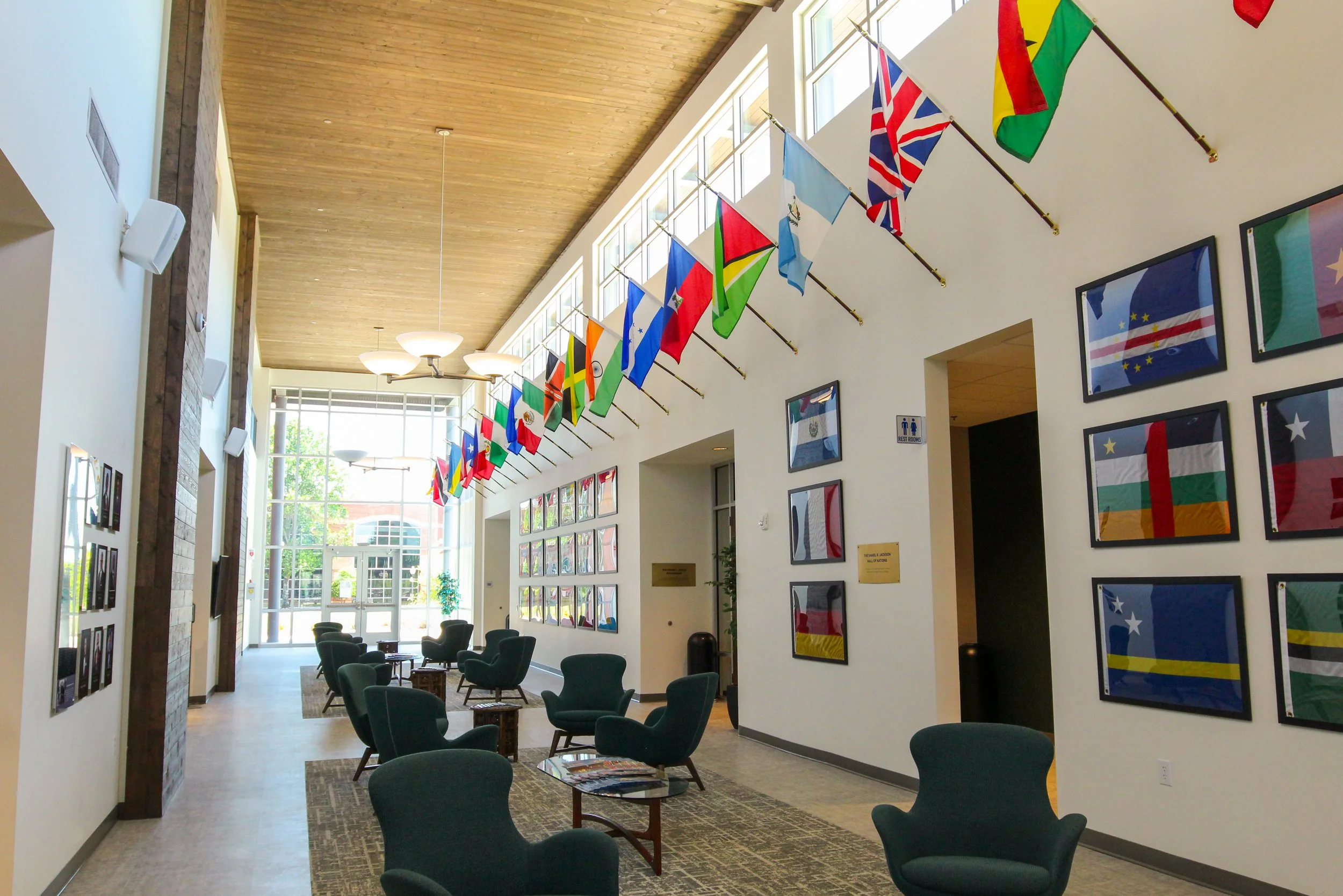 Interior of a modern building lobby with flags hanging from the ceiling and framed flag artwork on the walls, featuring seating areas with green chairs and large windows allowing natural light. Design, build by P&C Construction, Inc. -Chattanooga, TN