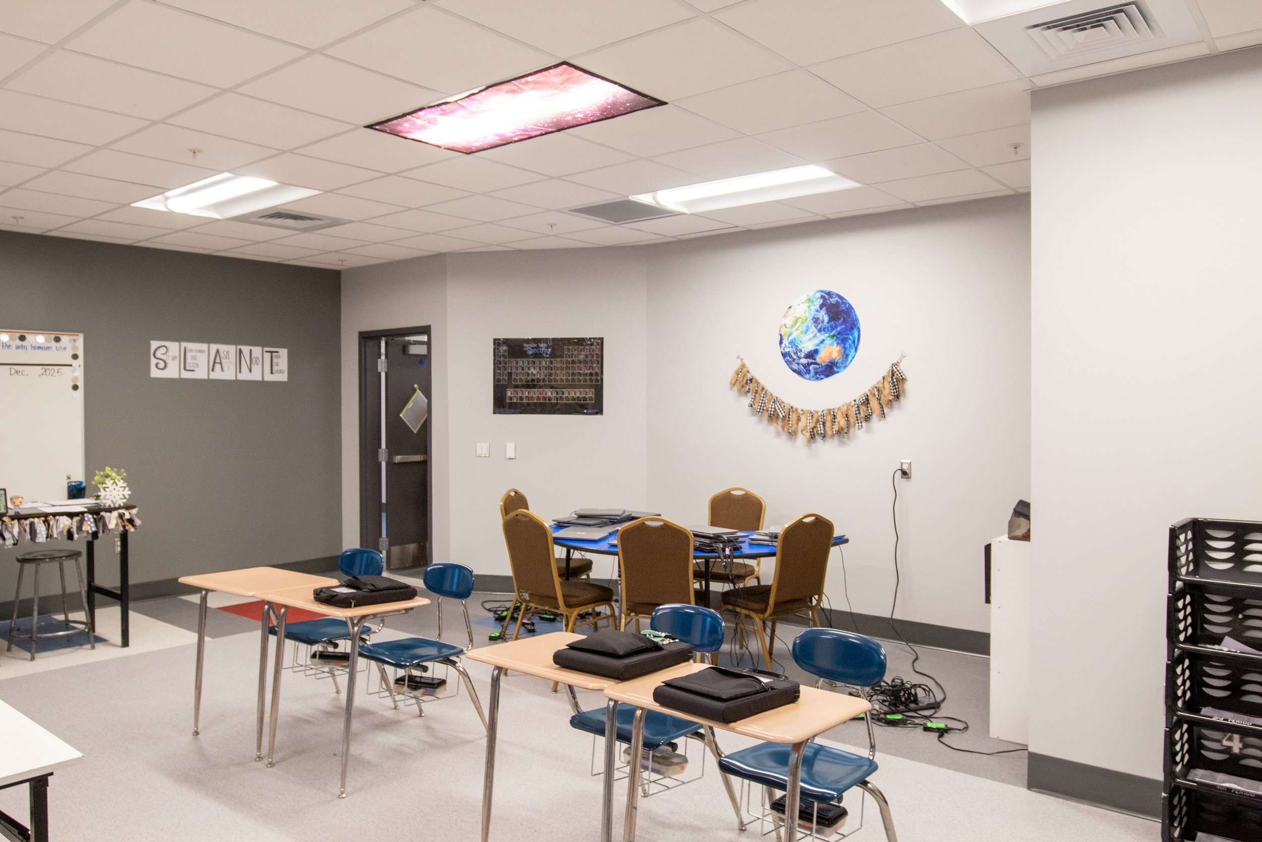 Classroom decorated for Earth Day with poster of Earth, garland, tables, chairs, and educational materials.