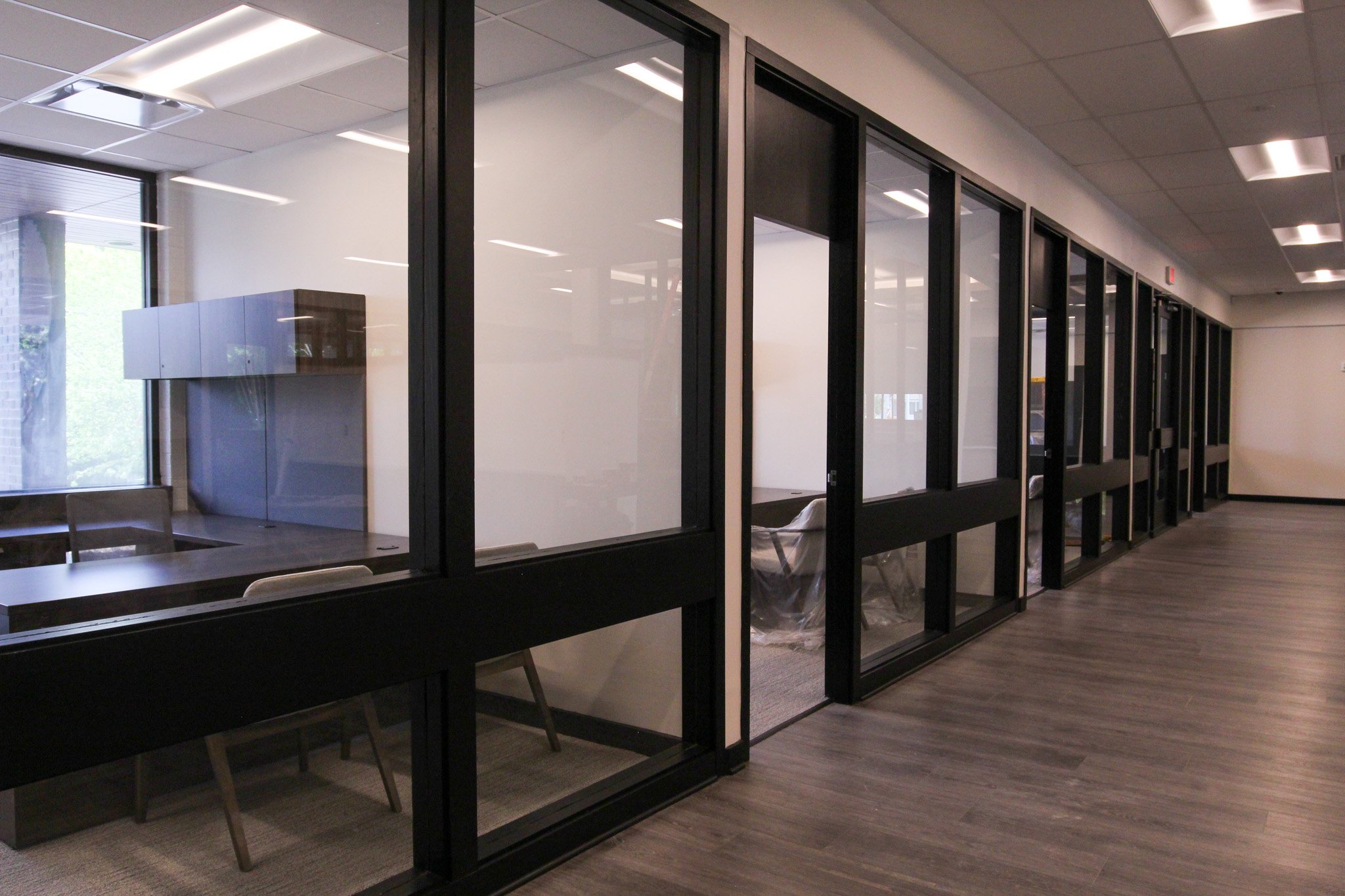 Office interior of Simmons Bank in Athens, TN with glass-walled partitioned rooms, a table with chairs, and ceiling lights.