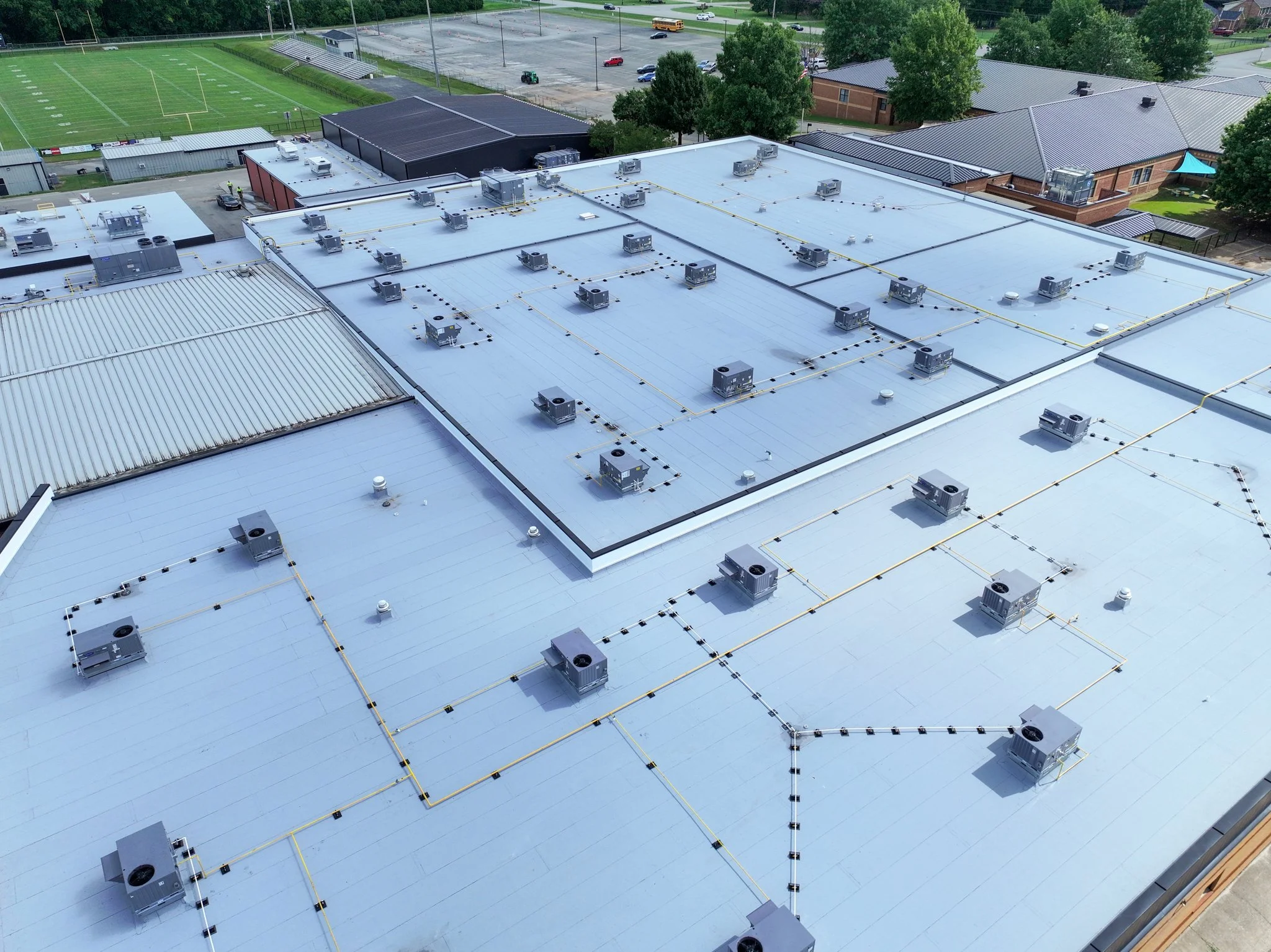 Aerial view of Discovery Middle School building rooftop with multiple HVAC units, surrounded by trees, sports field, parking lot, and nearby school buildings. Built by P&C Construction.