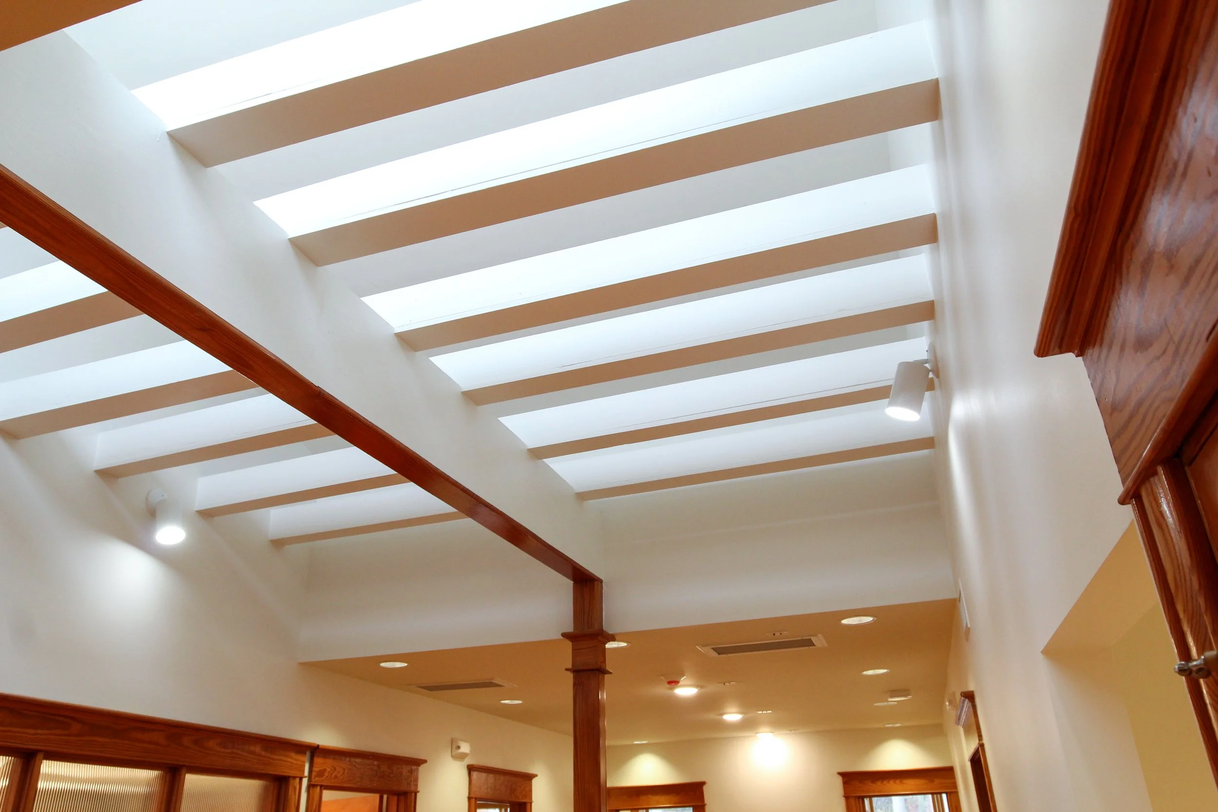 Interior view of a room with a skylight ceiling, wooden beams, and recessed lighting.