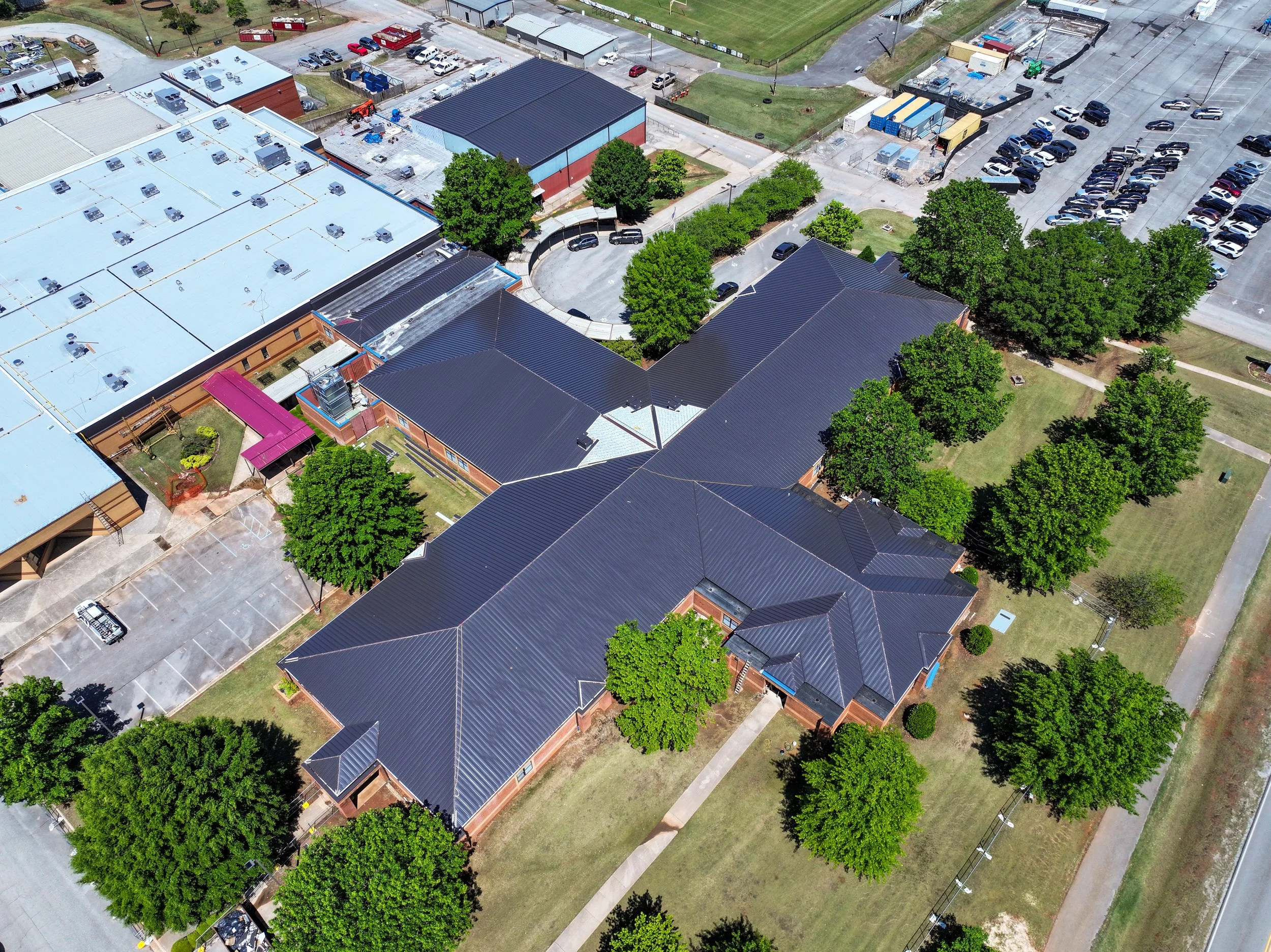 An aerial view of a school campus with multiple buildings with black and white roofs, trees, a parking lot partly filled with cars, and grassy areas. Remodeled by P&C Construction, Inc. - Chattanooga, Tn.
