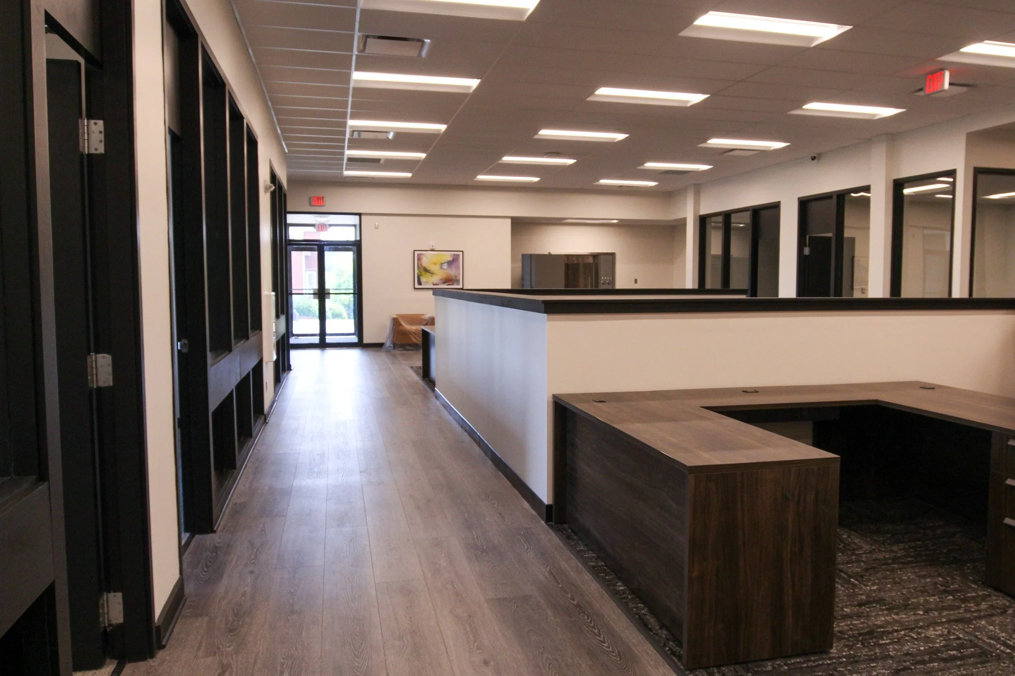 Empty modern office lobby of Simmons Bank in Athens, TN with wood flooring, large black-framed glass doors, a countertop reception area, and minimal wall decor.