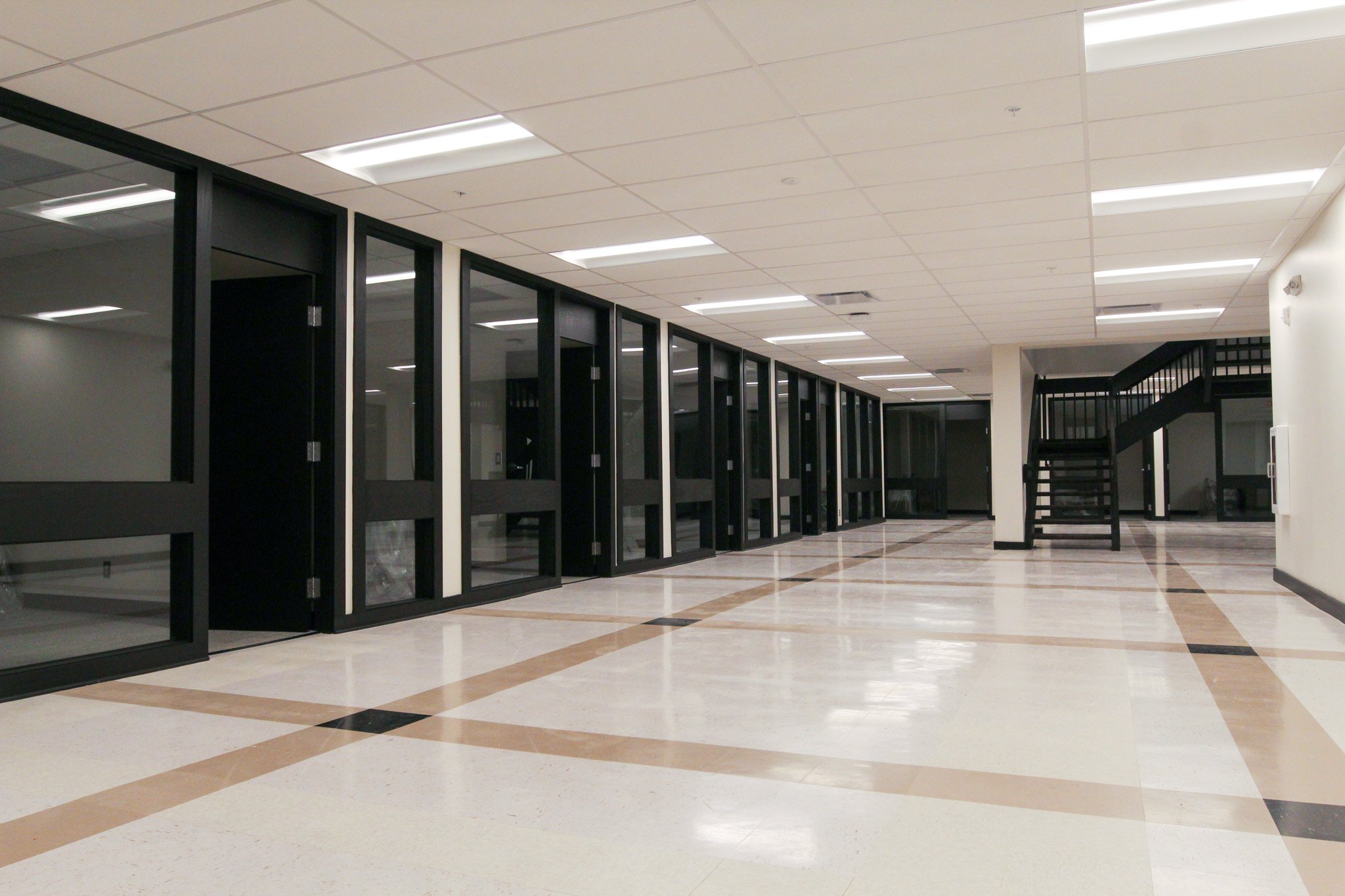 Empty hallway with black-framed glass doors and tiled flooring.