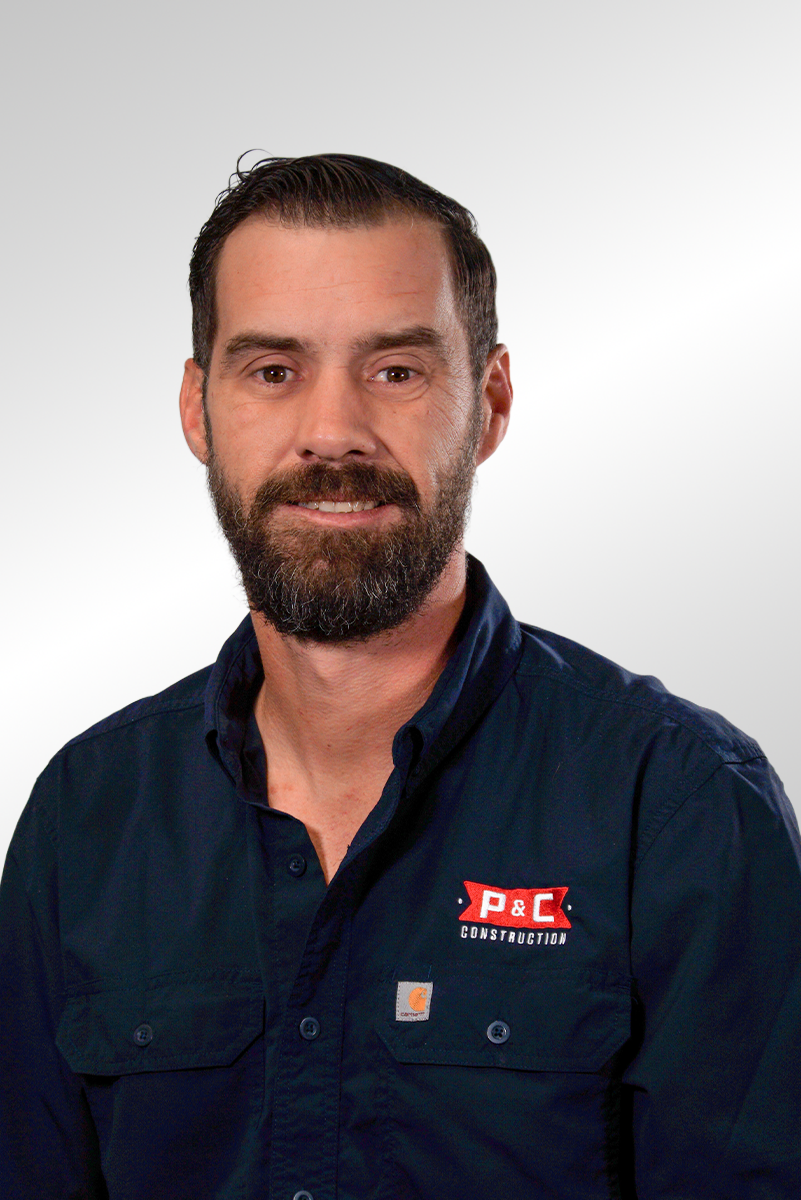 Headshot of a man with dark hair, a beard, wearing a dark blue shirt with a P&C Construction logo, against a plain light background.