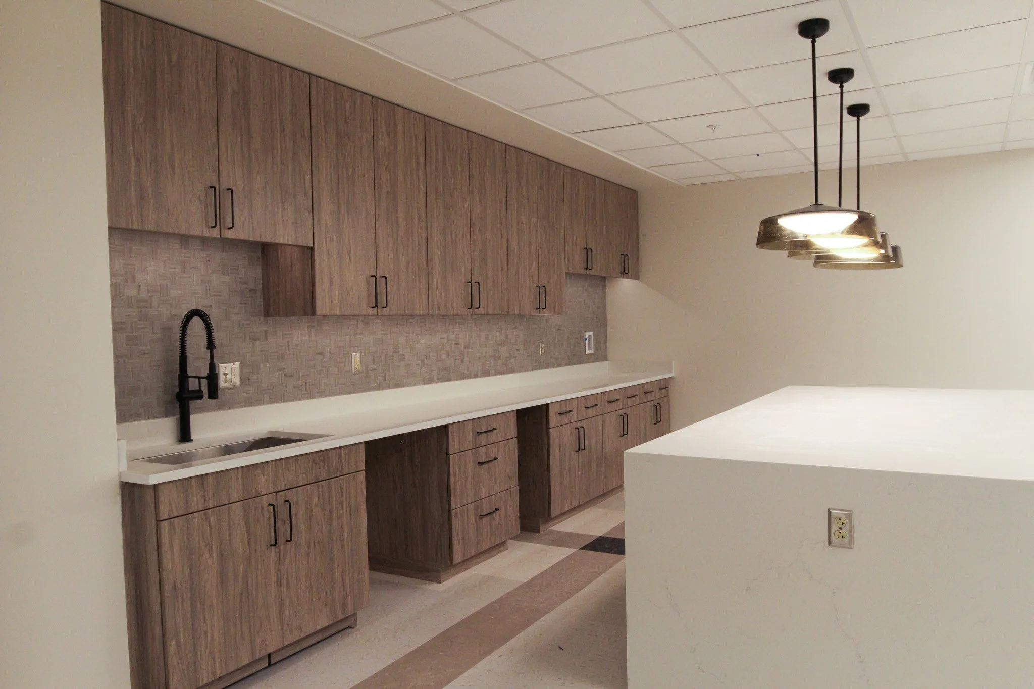 Modern kitchen with wood cabinets, black faucet, beige backsplash, white countertop, and pendant lights.