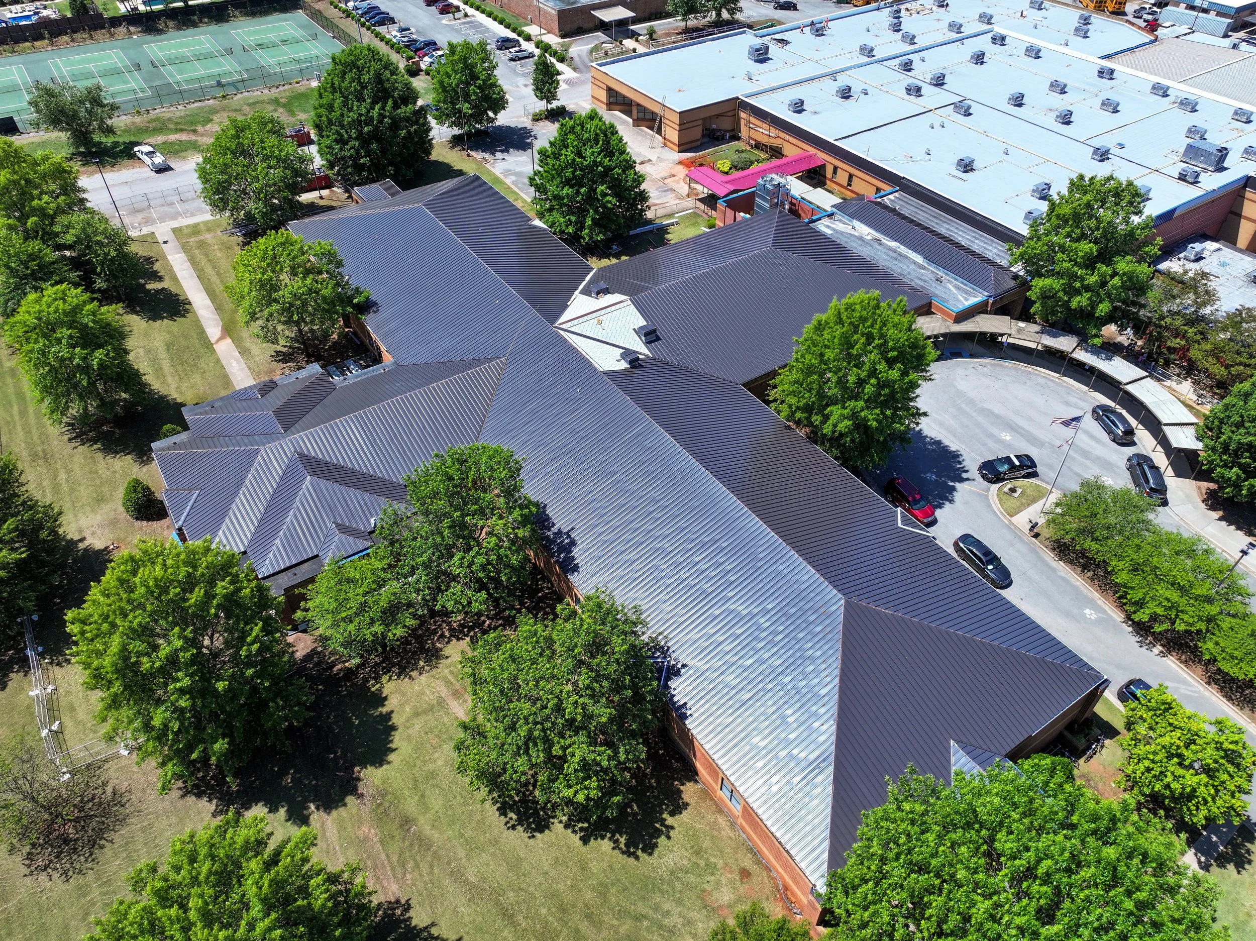 An aerial view of a school campus showing parking lots, a sports court, trees, and buildings with metal roofs. Remodeled by P&C Construction, Inc. - Chattanooga, Tn.