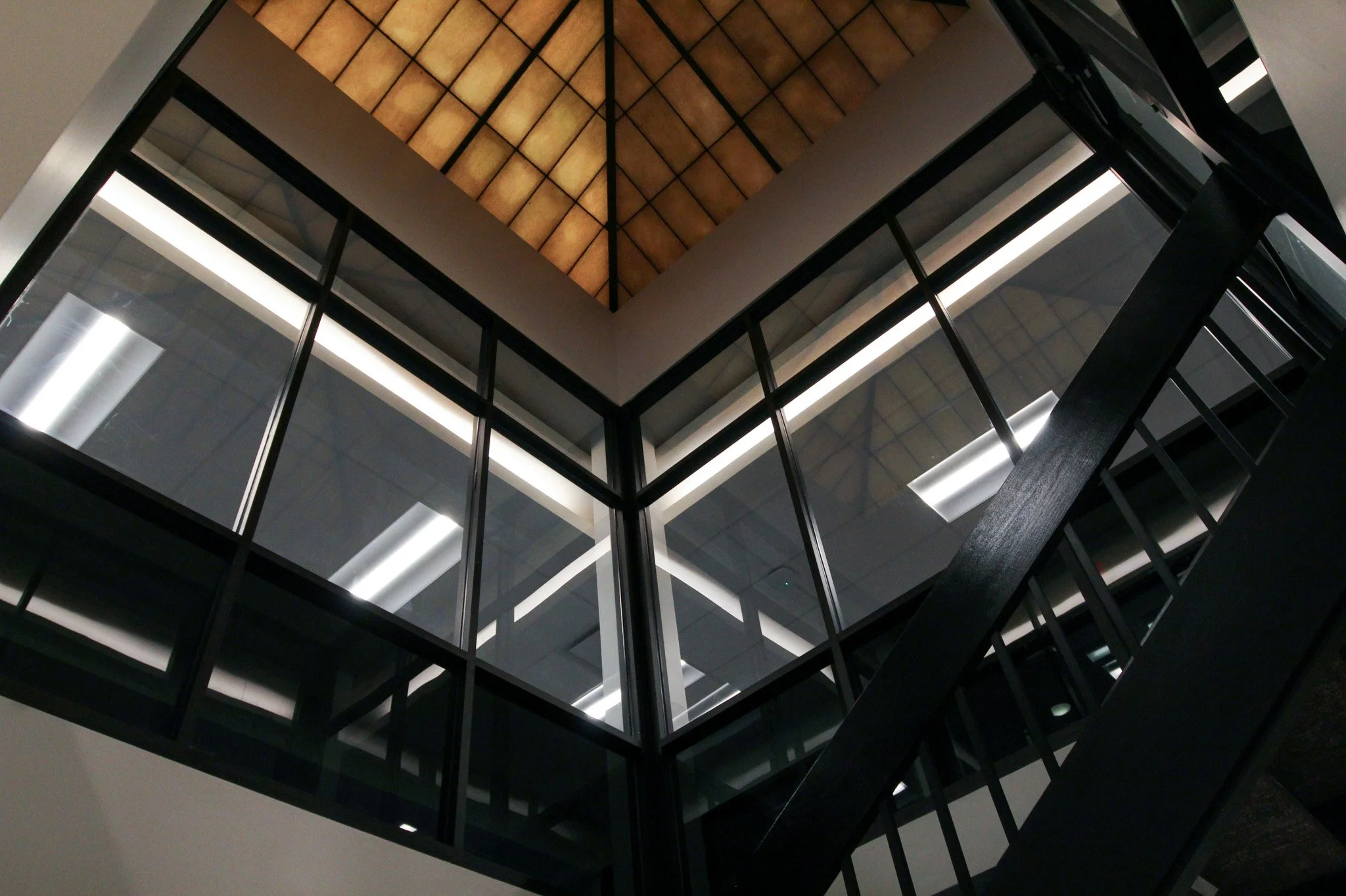 Interior view of a modern building with a glass ceiling and black framing, seen from below.