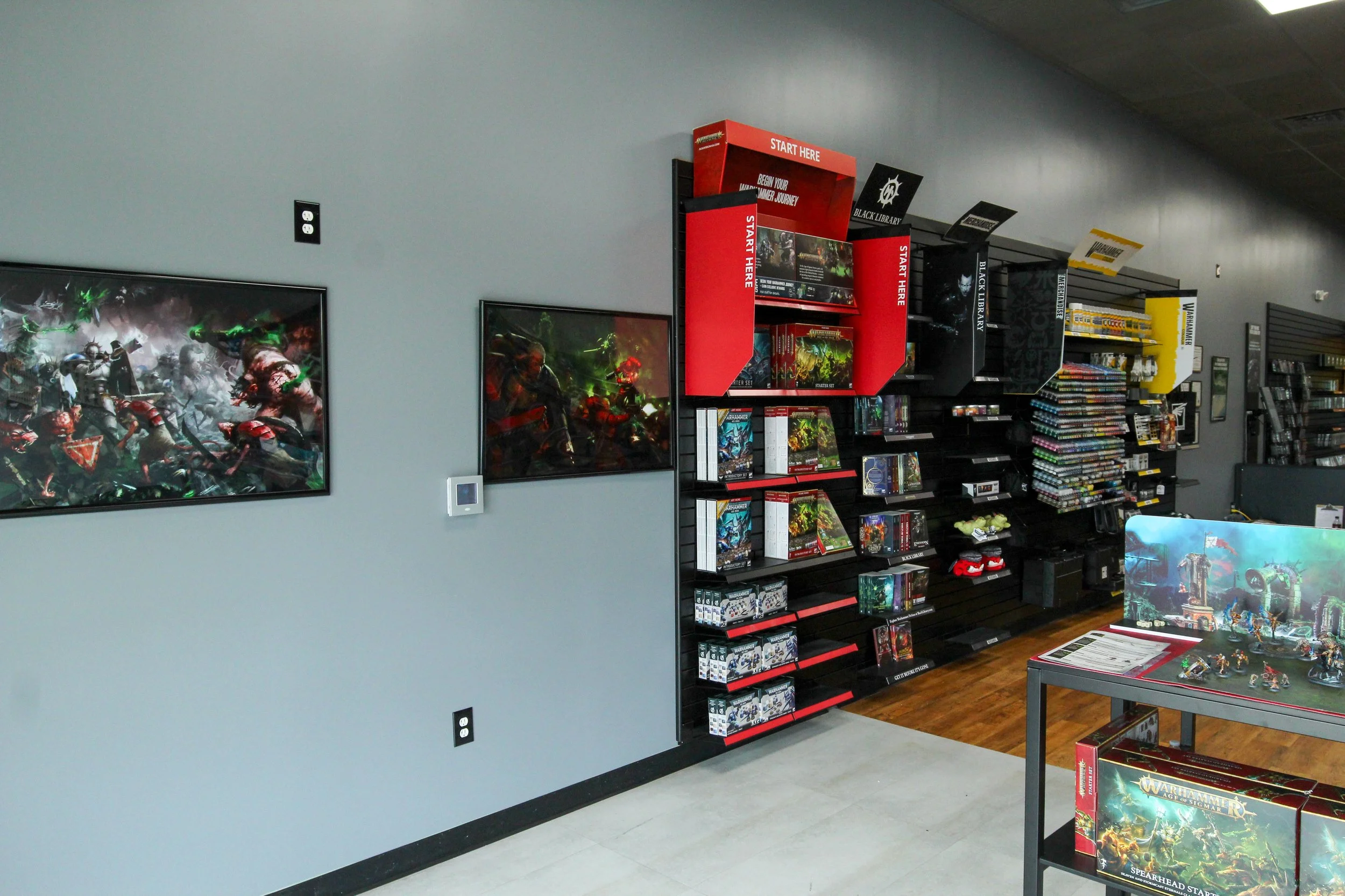 A store display with tabletop and shelves featuring tabletop miniatures, game boxes, and related merchandise, with advertising signage indicating sections for Warhammer and other tabletop games. Remodeled by P&C Construction, Inc. - Chattanooga, Tn.