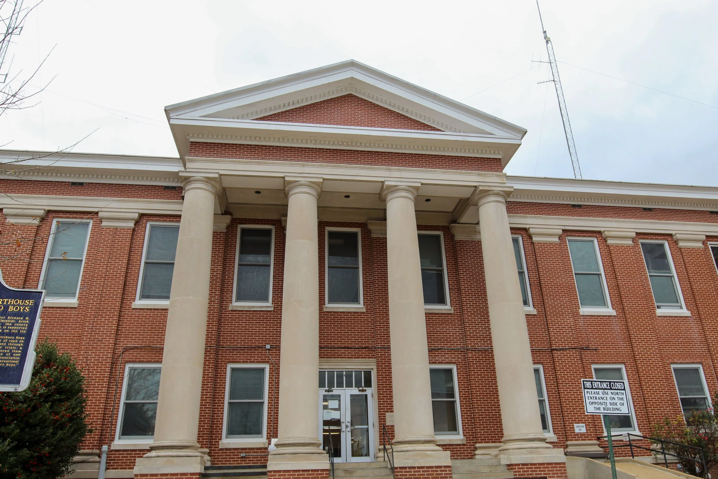 Brick building with large pillars at the entrance, multiple windows, and a triangular pediment on top. Sign indicating entrance is closed.