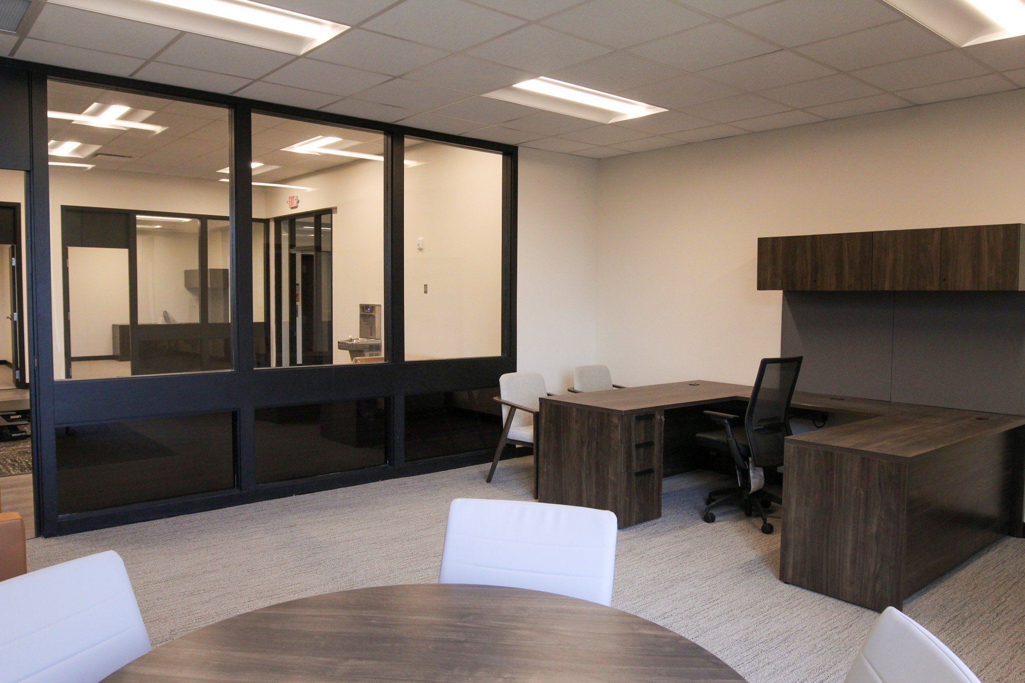 An office conference room of Simmons Bank in Athens, TN with a modern decor, including white chairs, wooden desks, a glass wall, and ceiling lights.