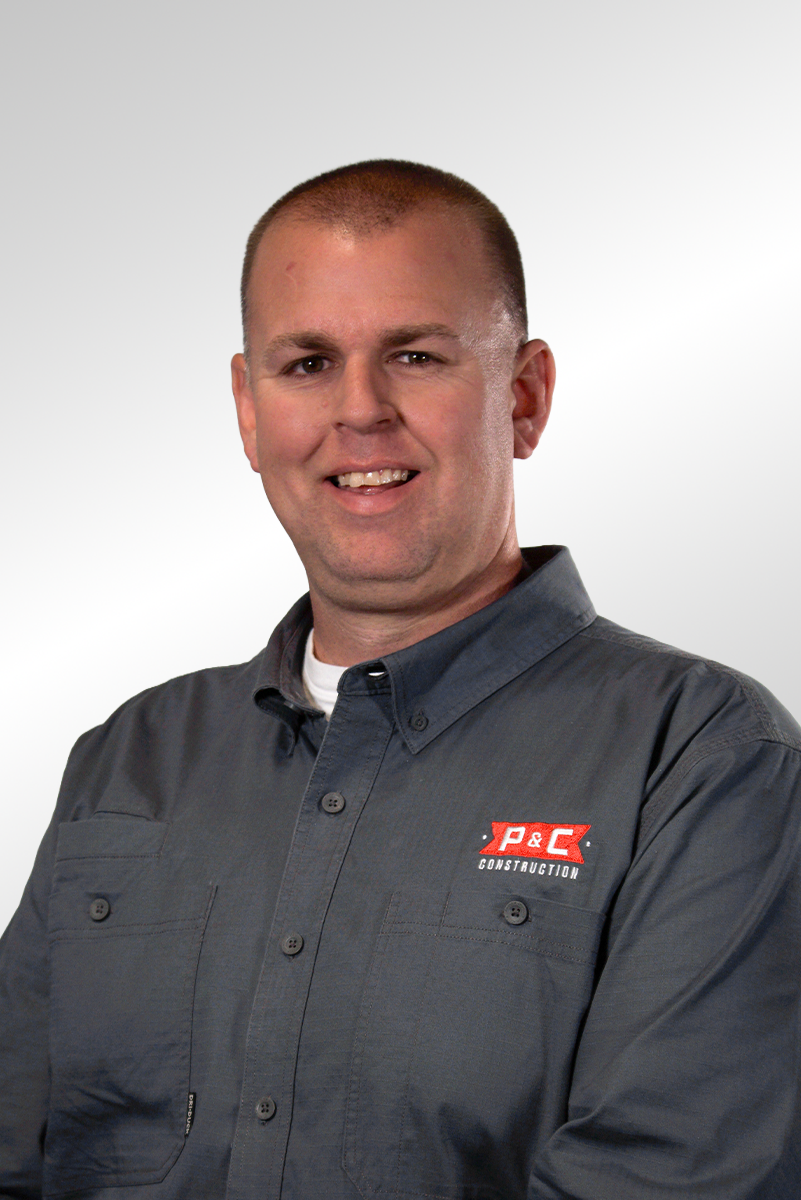 A man wearing a brown collared shirt with a 'P&C Construction' logo, standing against a dark background.
