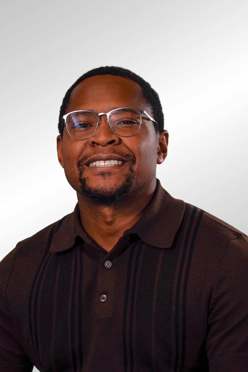 Smiling man wearing a light blue work shirt with P&C Construction logo, standing against a dark background.