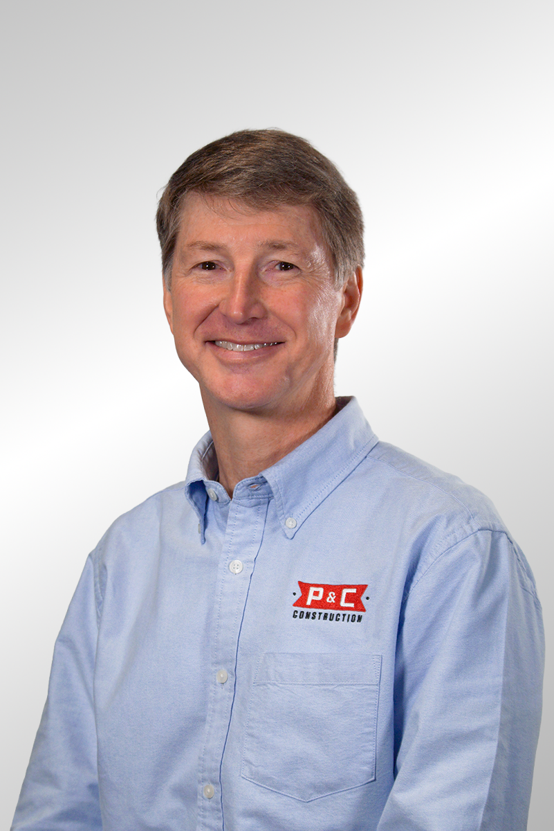 A man with brown hair wearing a blue and white checkered button-up shirt posing against a gray background.