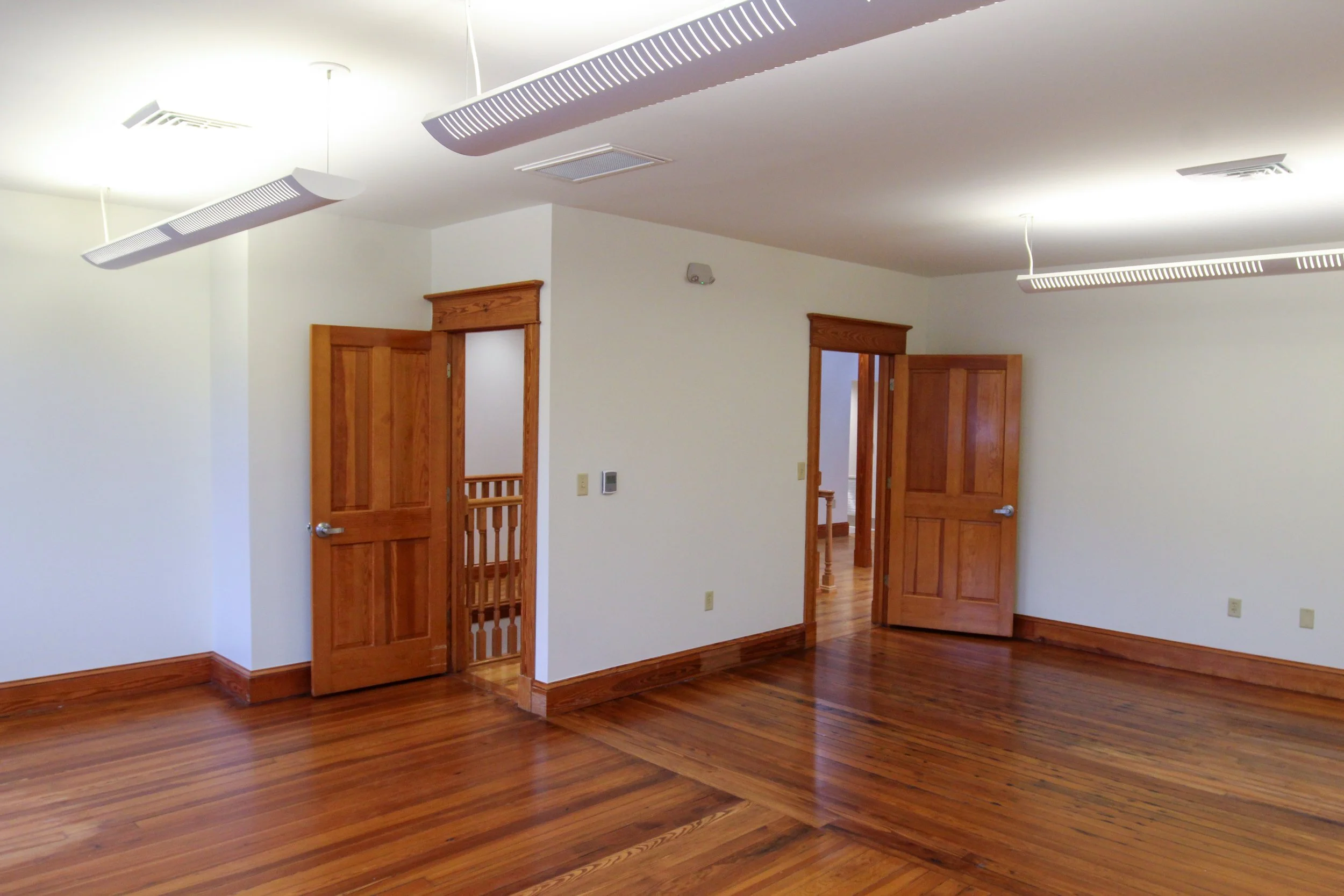 Empty room with hardwood floors, white walls, wooden doors, and ceiling lighting fixtures.