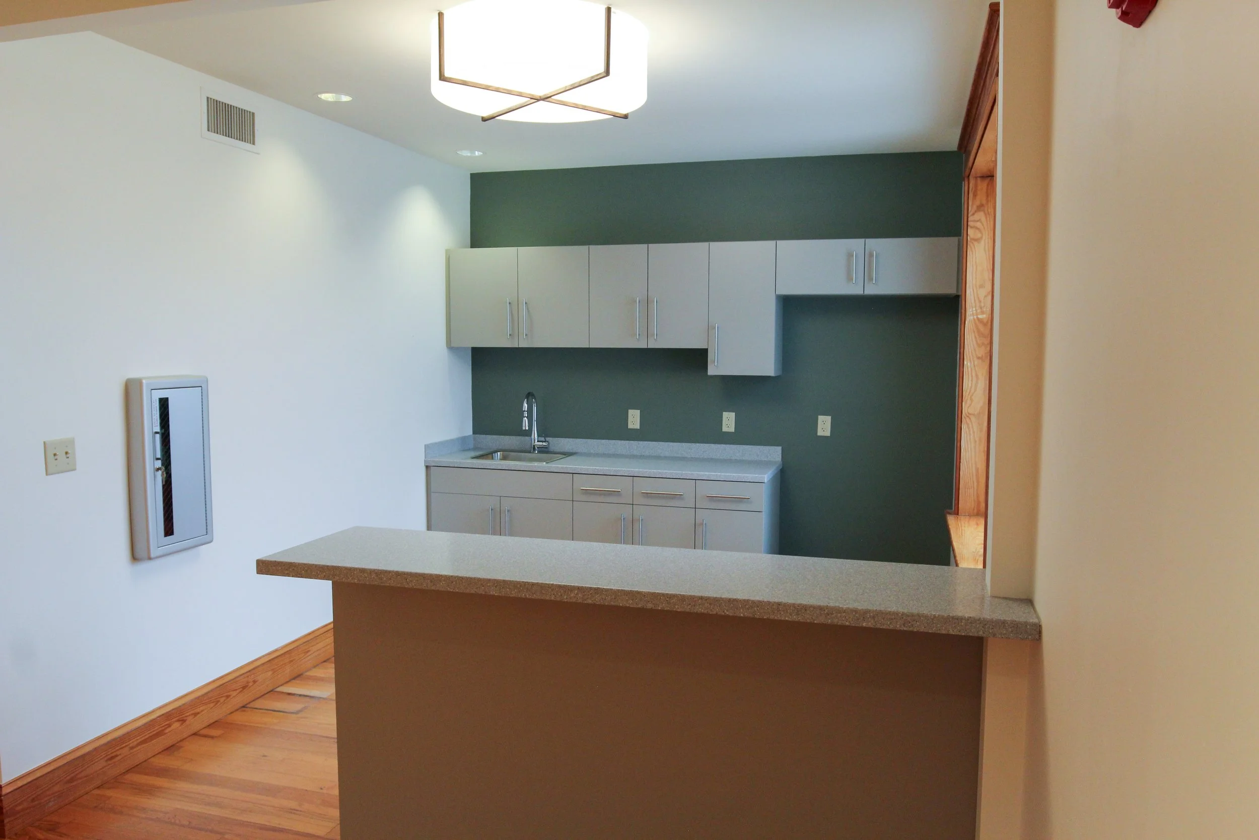 Empty kitchen with beige cabinets, a green accent wall, a single-basin sink, and a wooden floor.