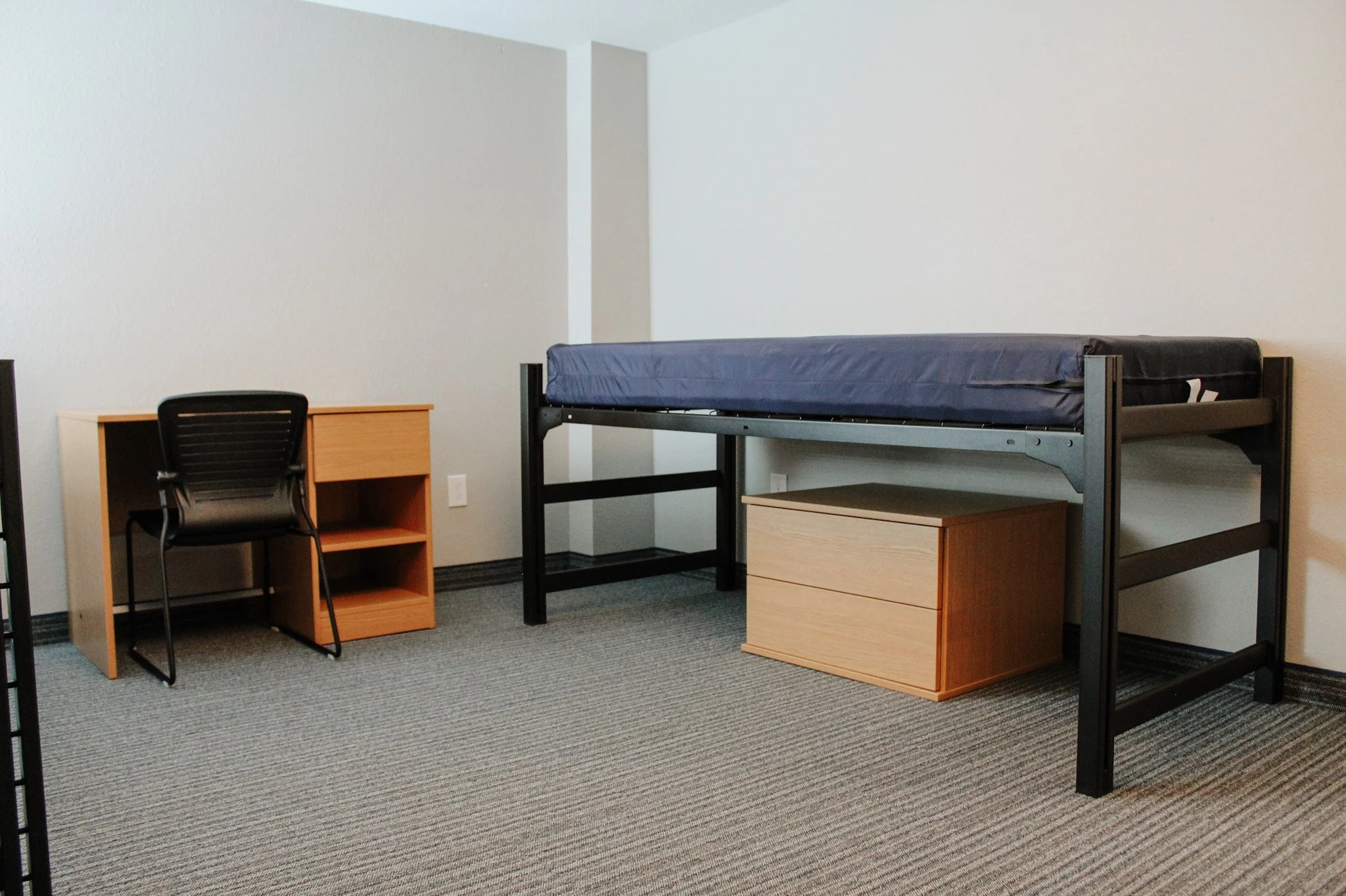A room with a bed, two wooden nightstands, a desk, and a black chair. The room has white walls and gray carpeting. Remodeled by P&C Construction, Inc. - Chattanooga, Tn.