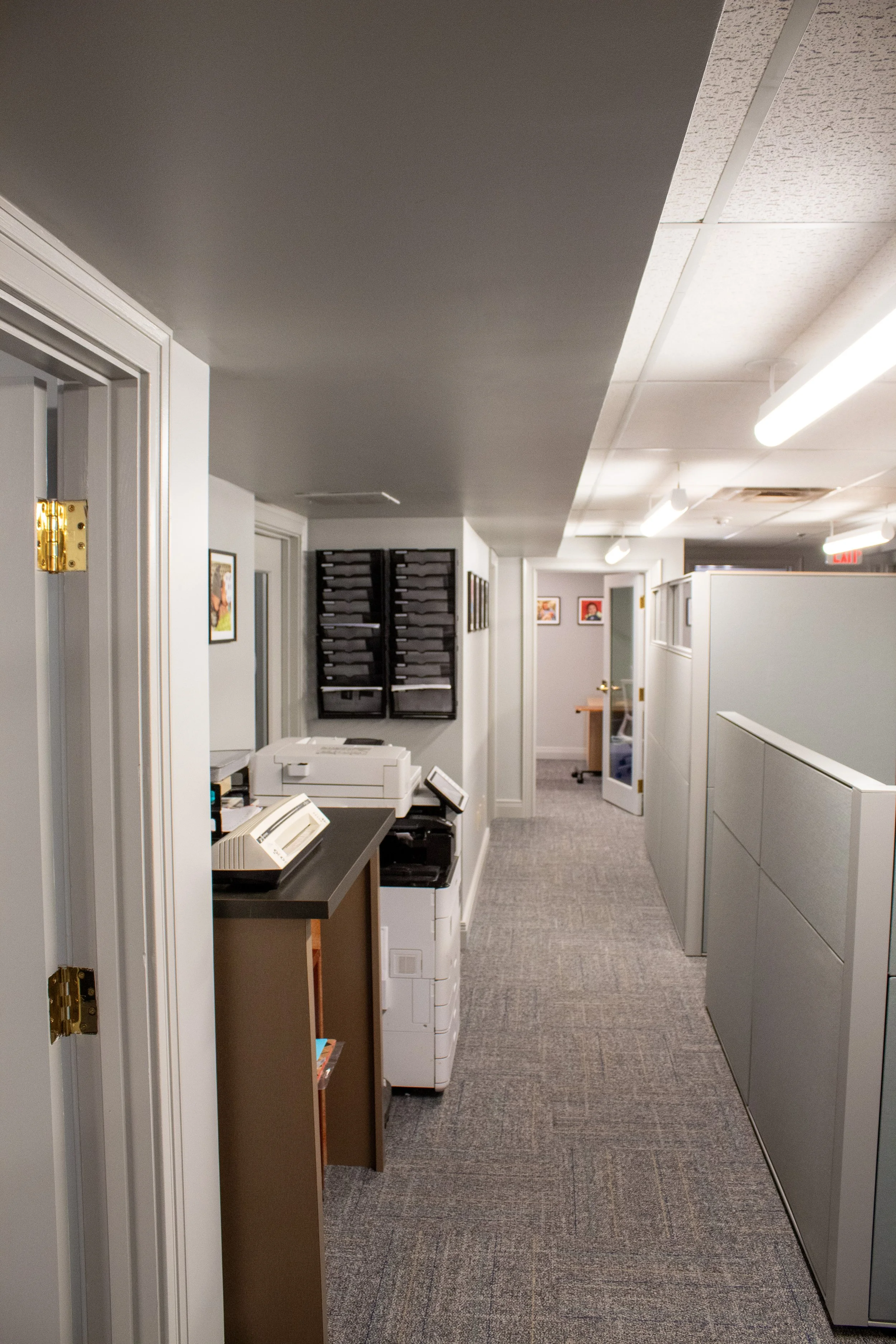 Office hallway with cubicles, printers, and framed artwork on the walls.