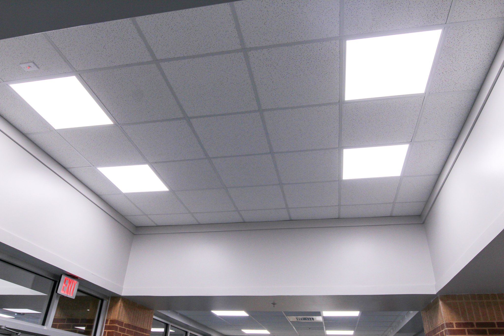 Ceiling with fluorescent lights and an exit sign in a building corridor.