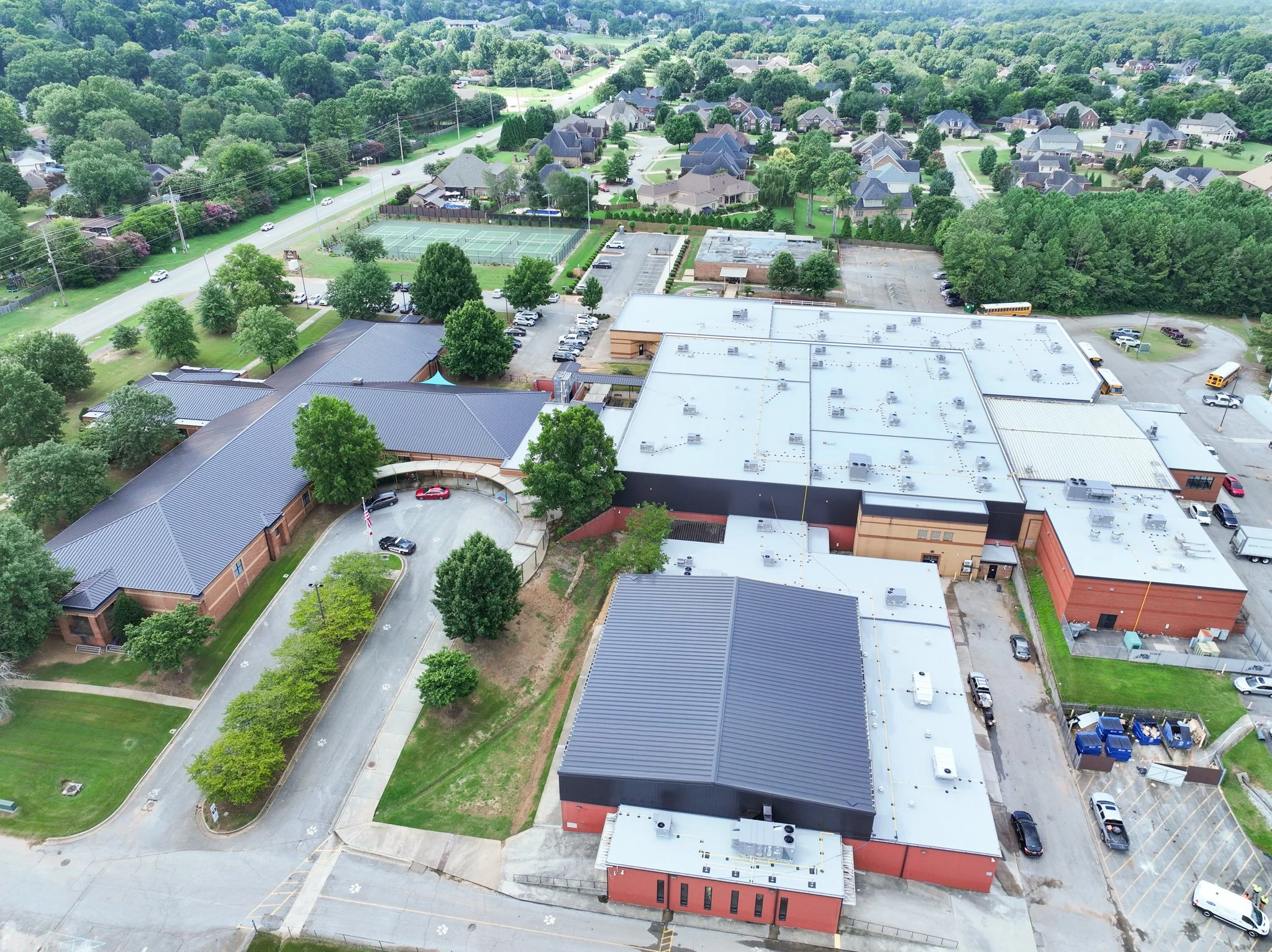 Aerial view of  Discovery Middle School with houses, green trees, a parking lot, tennis courts, and surrounding greenery.