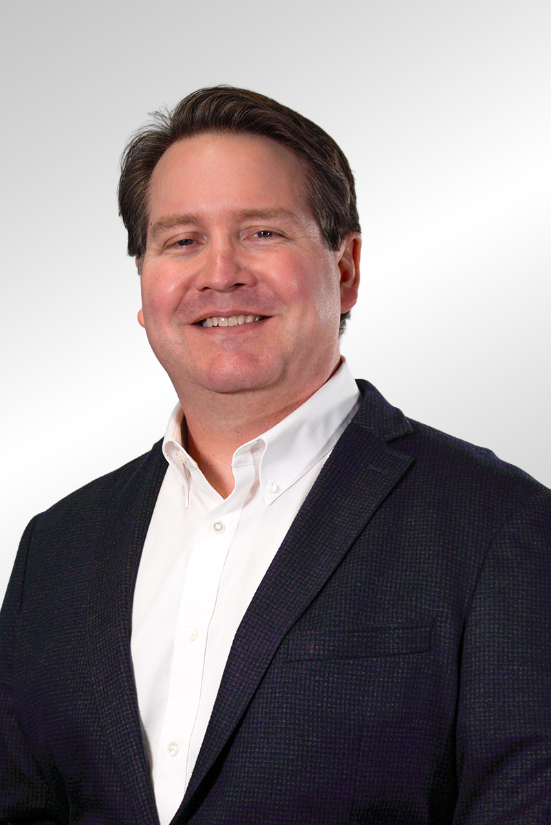 Headshot of a man with brown hair wearing a beige collared shirt with a PEC Construction logo on the front pocket, smiling against a gray background.