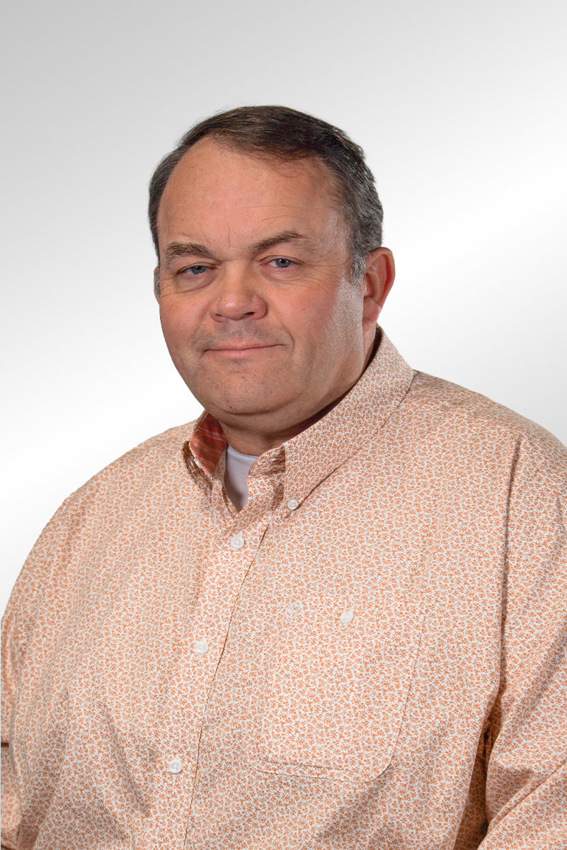 Man with short brown hair wearing a plaid shirt with a P&L Construction logo, smiling against a gray background.