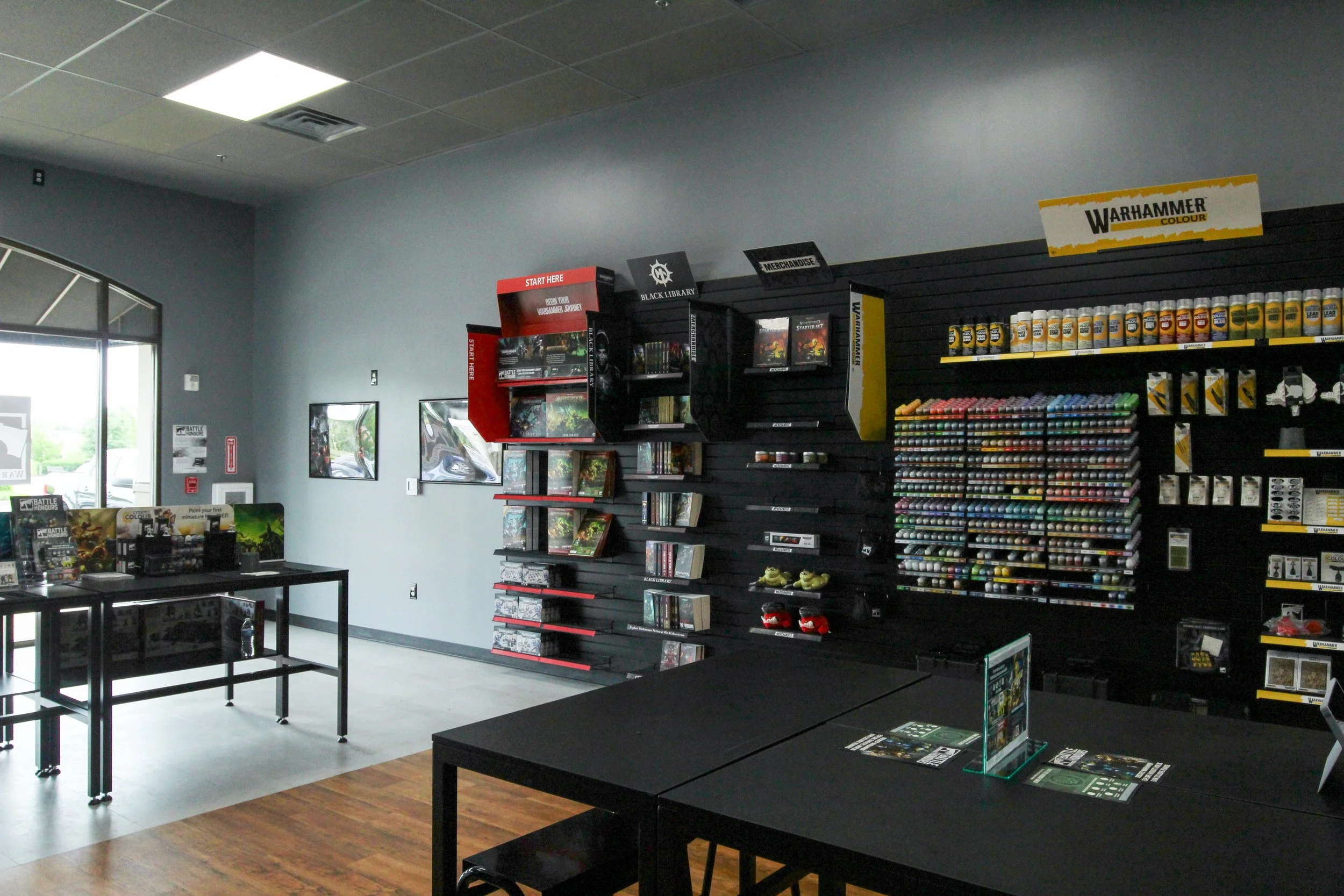 Inside a retail store with shelves stocked with Warhammer merchandise, paints, and tabletop gaming supplies. There are tables and display areas, with bright natural light coming from large windows. Remodeled by P&C Construction, Inc. - Chattanooga.