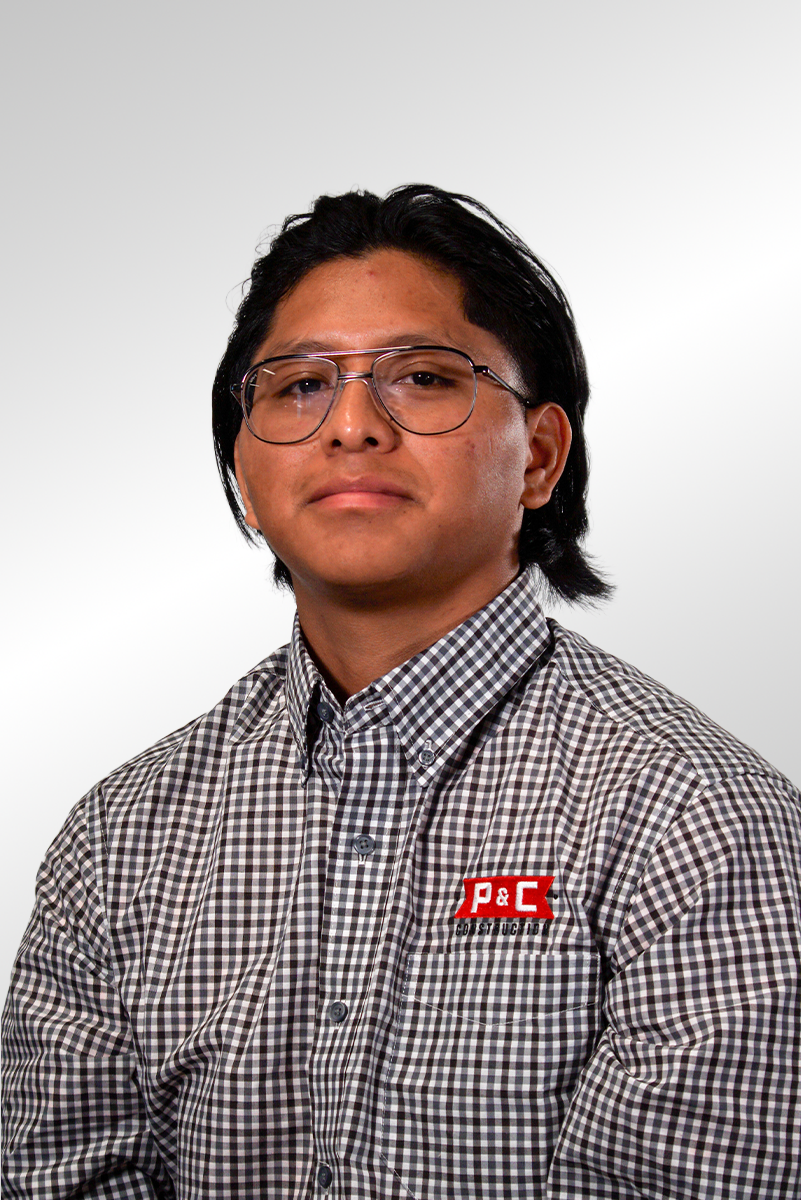 A young man with short, dark hair and a serious expression, wearing a gray button-up shirt with a P&C Construction logo.