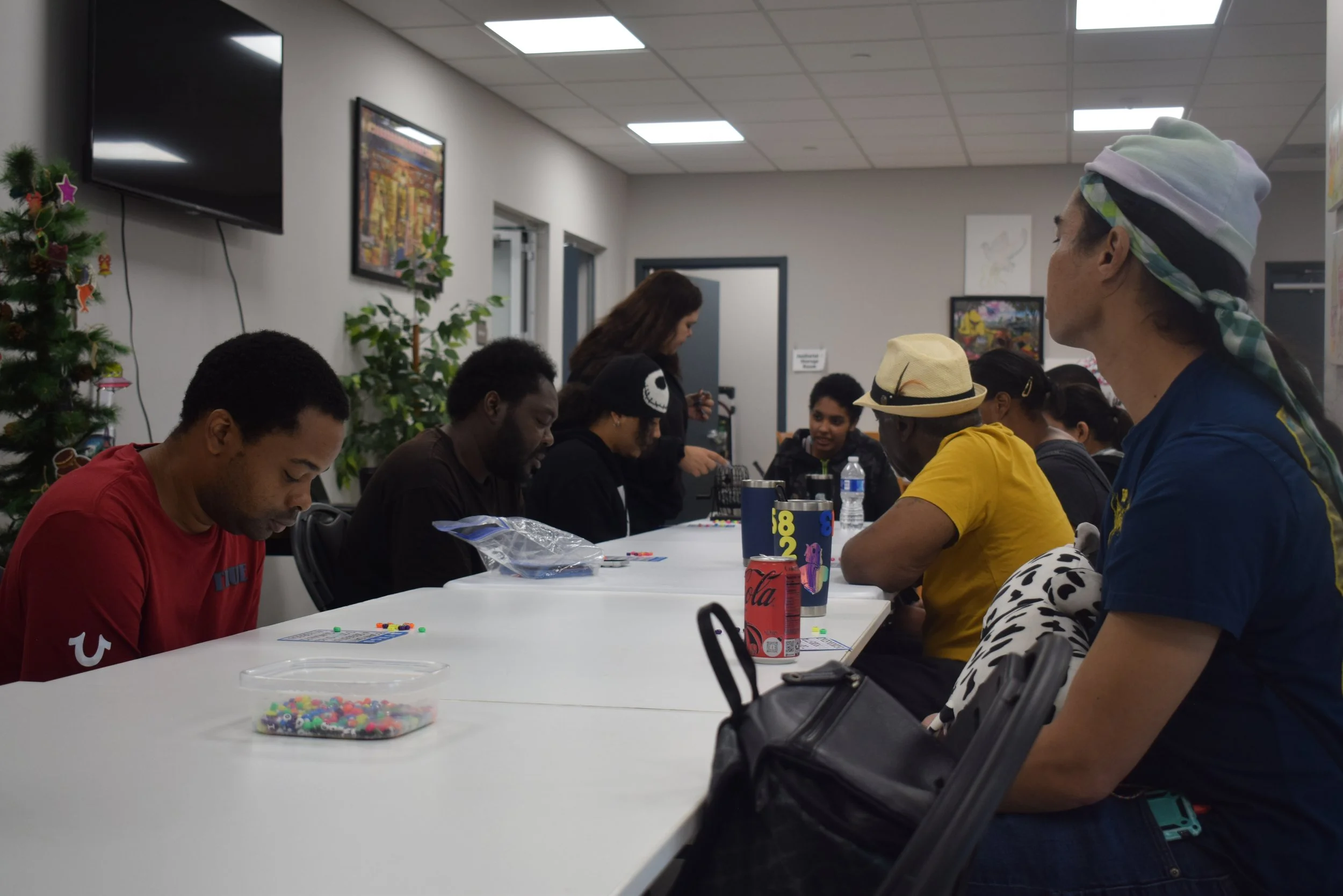 People sitting around a table playing a game, with cards, beads, and drinks on the table, in a room decorated with Christmas decorations.