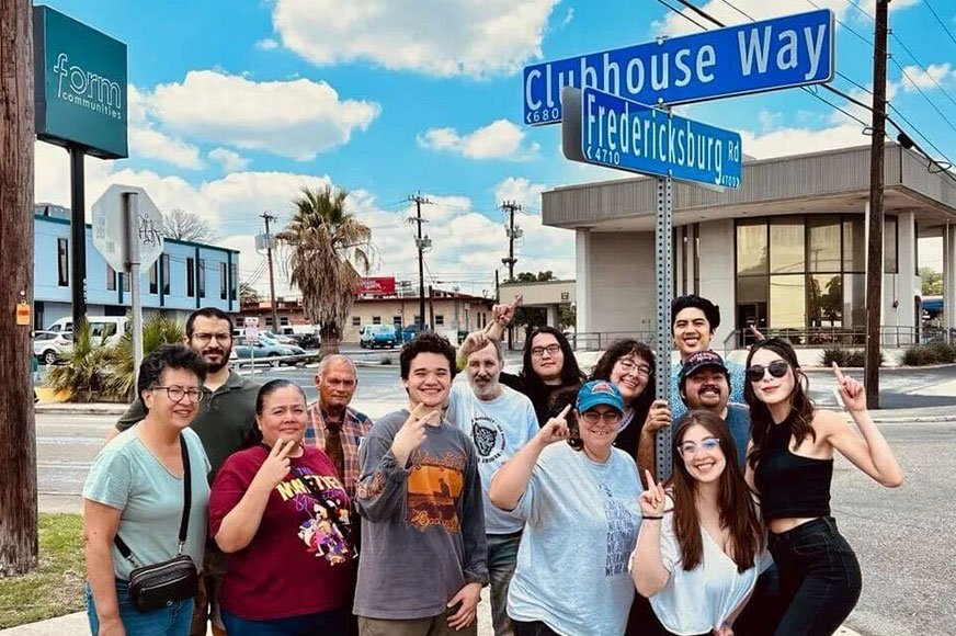 A group of people standing at the corner of Clubhouse Way and Fredericksburg Road, smiling and posing for a photo on a sunny day.