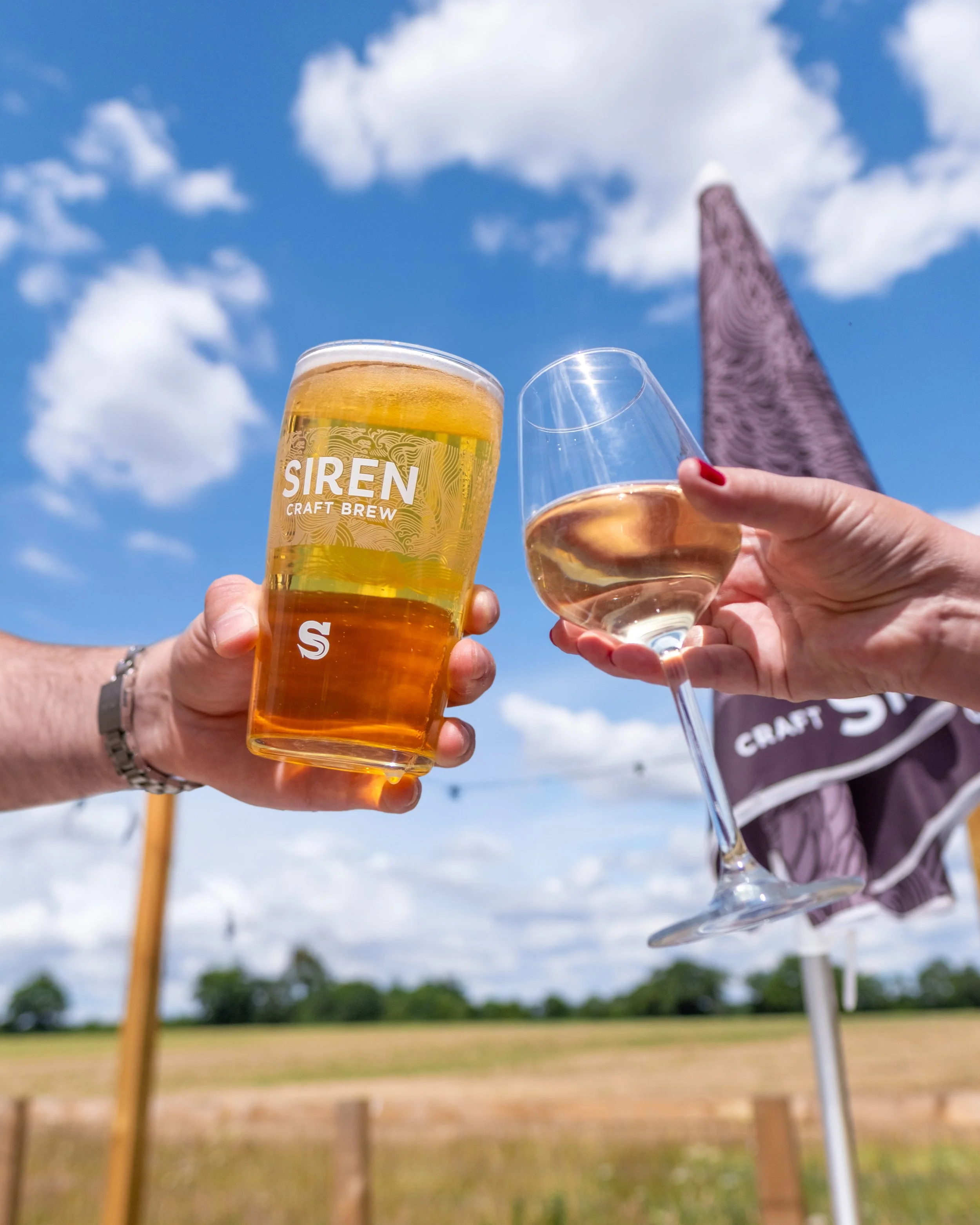 A pint of Siren Craft Brew lager and a glass of white wine cheersing in the sun at the George and Dragon, Swallowfield, Berkshire