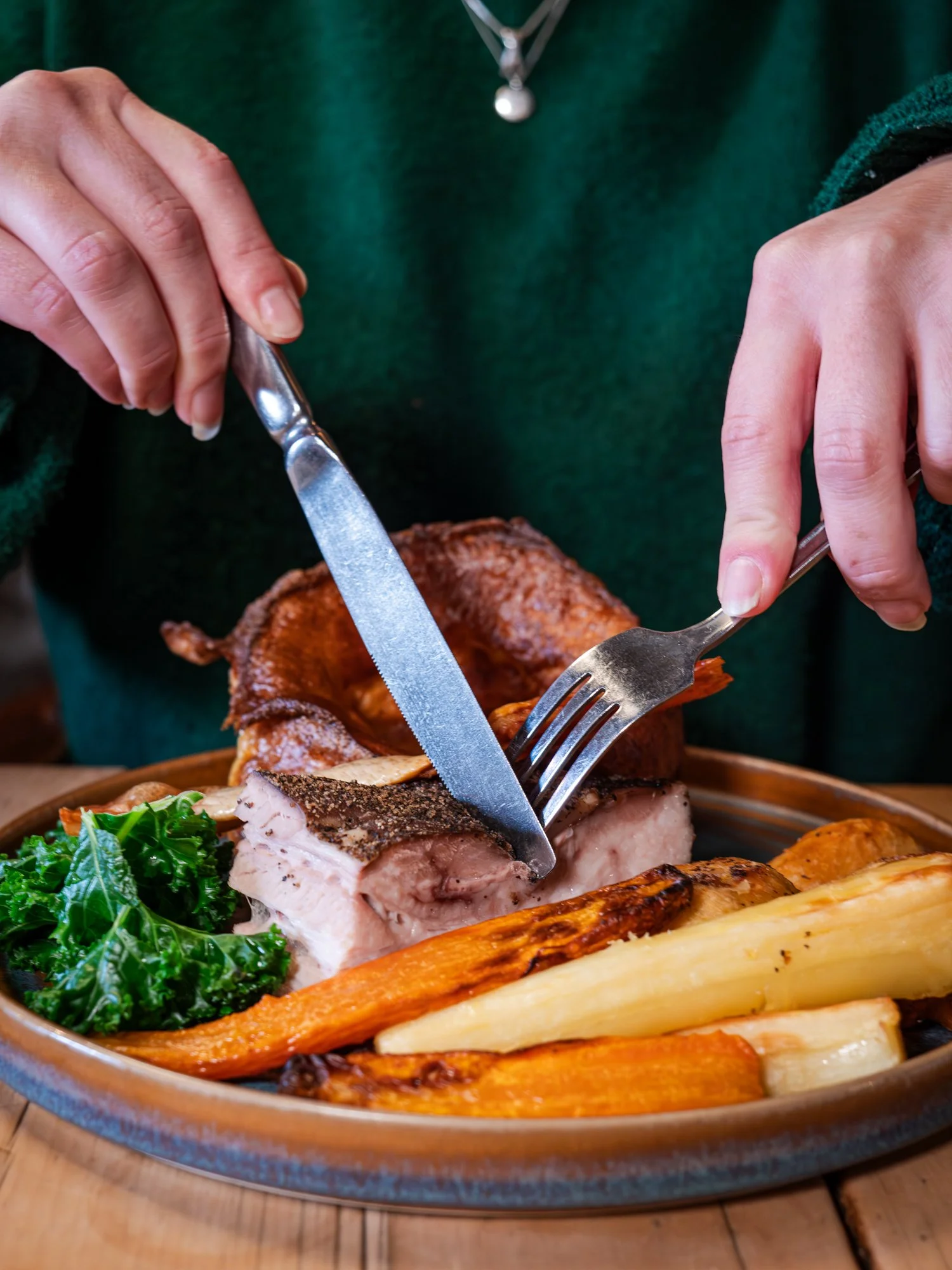 Person cutting a roasted pork dish with vegetables on a plate.