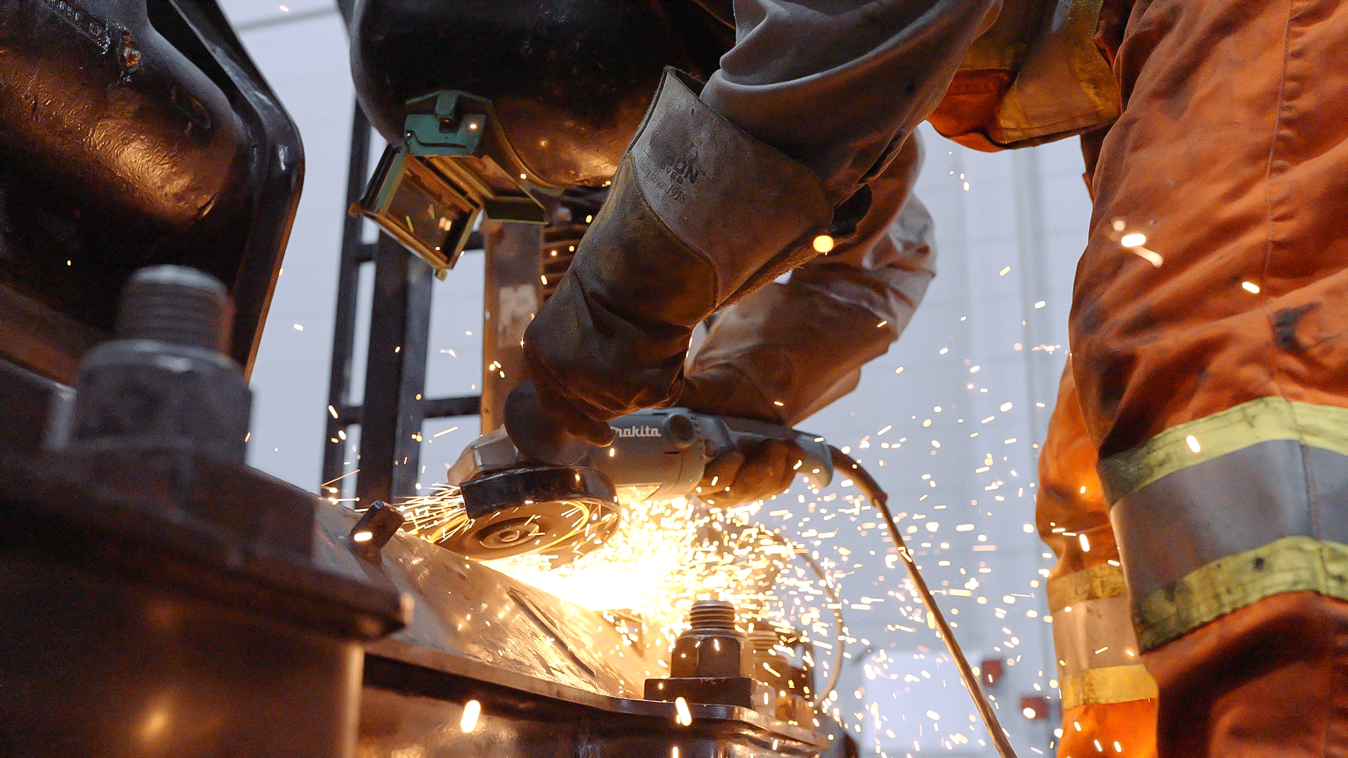 An employee at Breakthrough Industrial Solutions is welding and repairing a machine while wearing protective gloves and an orange jacket.