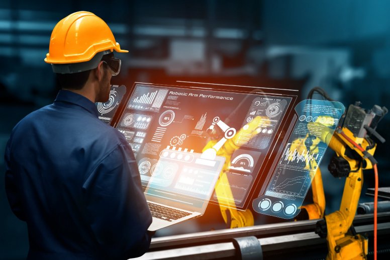 Engineer wearing safety helmet and glasses working with robotic arm and advanced digital interface.