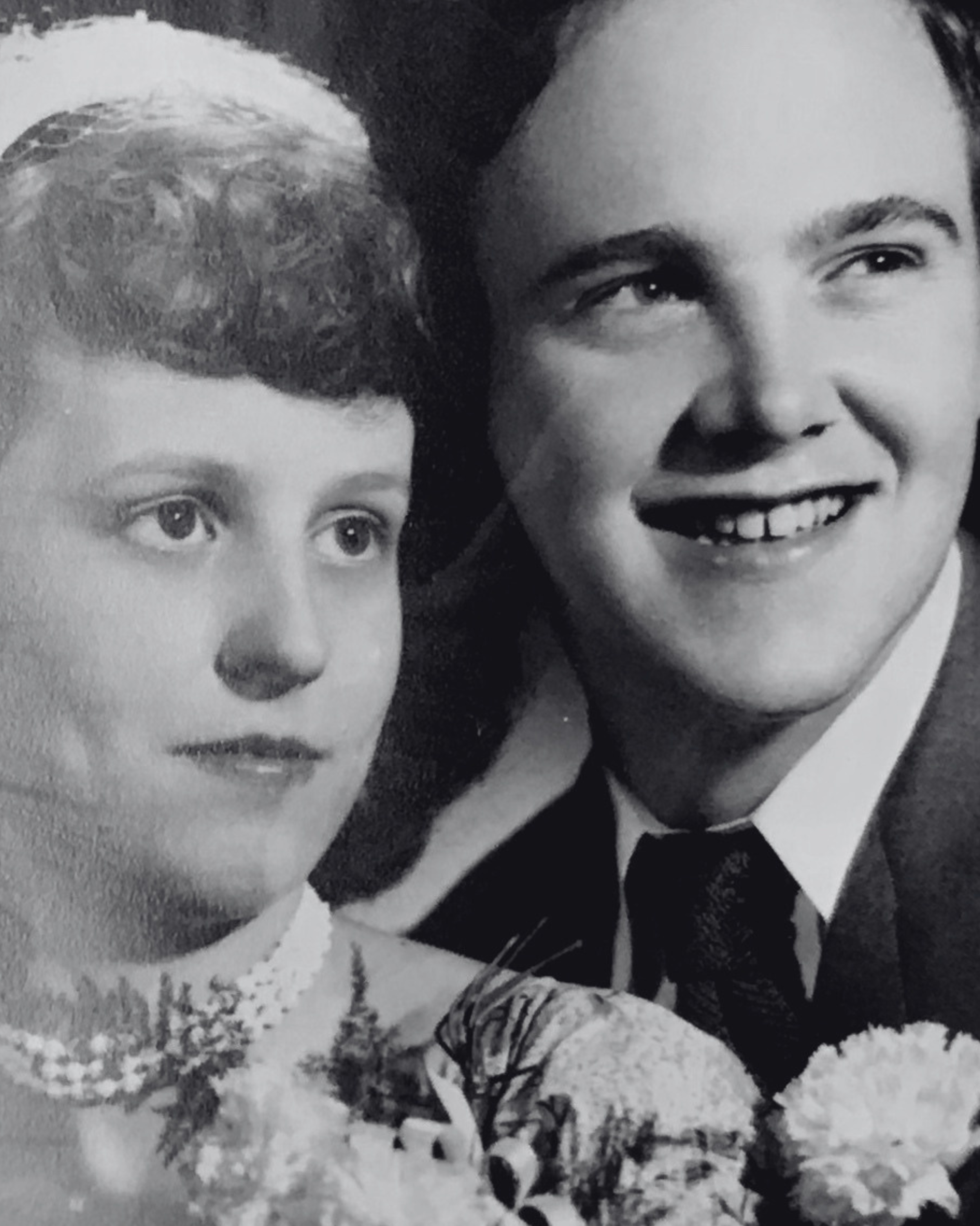 A black and white photograph of a woman and a young boy outside in snow. The woman has dark hair, is smiling, and is wearing a coat, while the boy has curly hair and is wearing a coat and boots. They are surrounded by snow-covered ground and trees in the background.