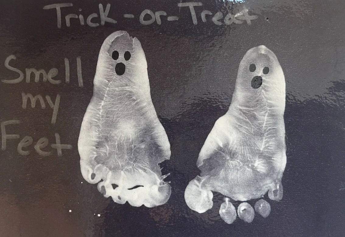 Footprints decorated for Halloween with black eye and mouth cutouts, labeled as 'Trick-or-Treat' and 'Smell my Feet' on a black background.