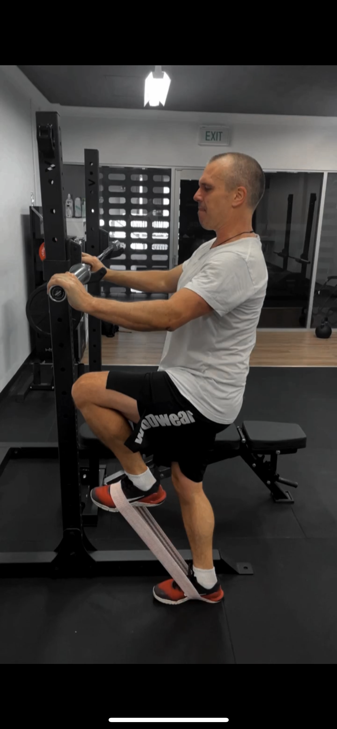 A man exercising in a gym, sitting on a bench and using elastic resistance bands around his ankle for leg workout. Redemption Training small group fitness and strength/cardio gym in Albion, North Brisbane. For all ages including over 40.