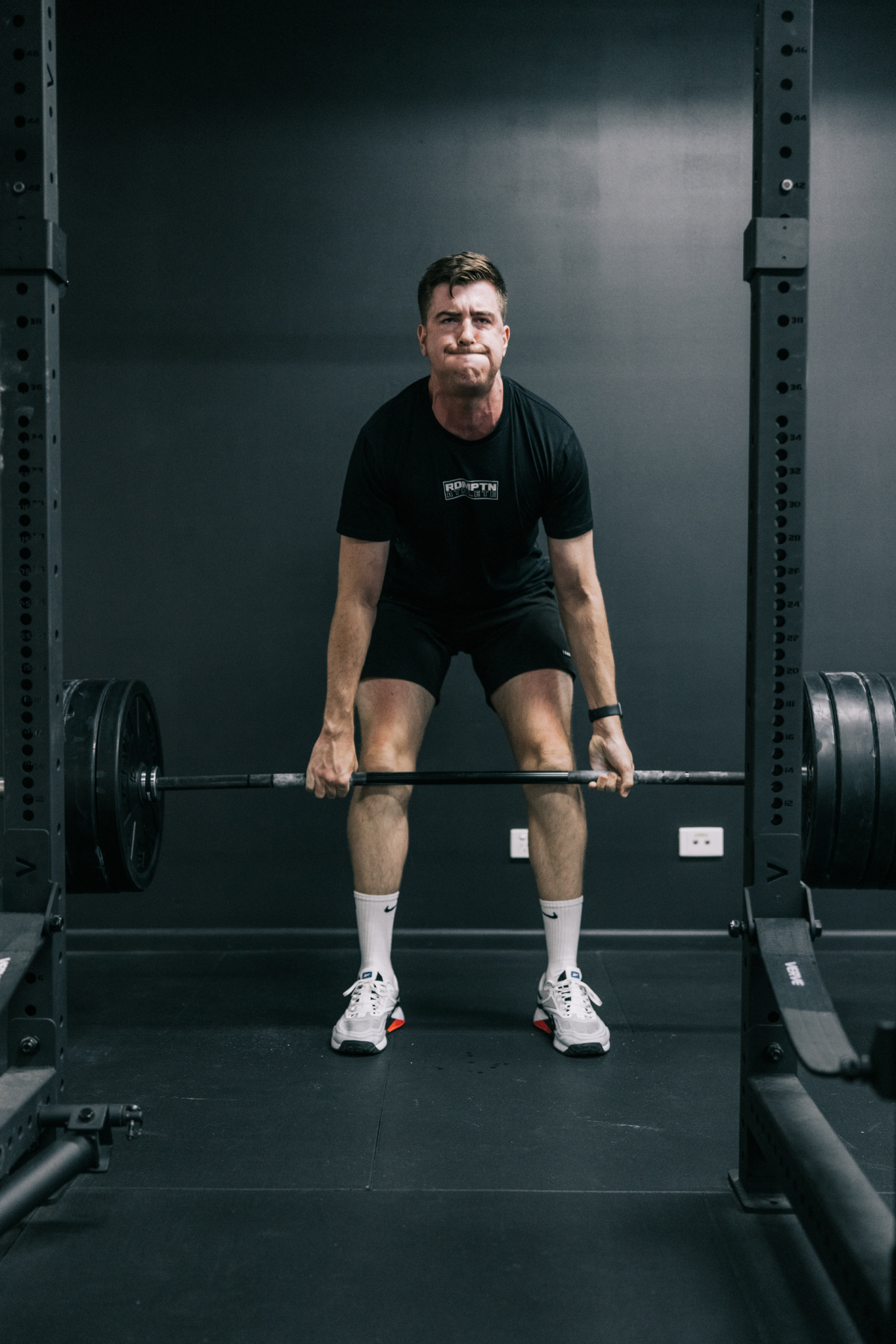 A man preparing to lift a loaded barbell in a gym with a black wall background. Redemption Training Albion, North Brisbane Small group fitness, strength and cardio gym.