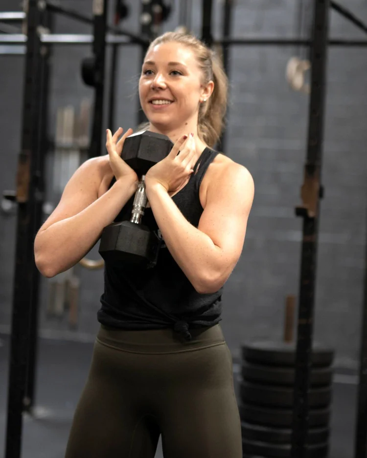 A woman smiles while holding a dumbbell at her chest