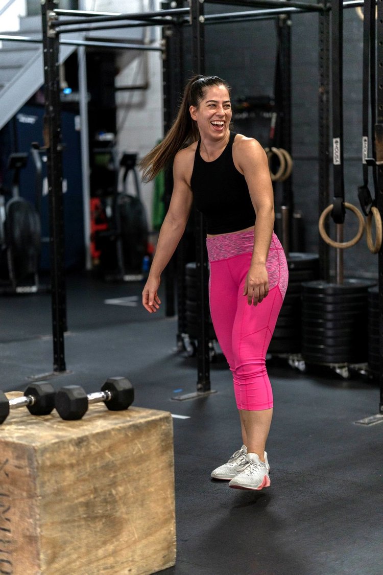 A woman laughs beside a box and dumbbells during a session