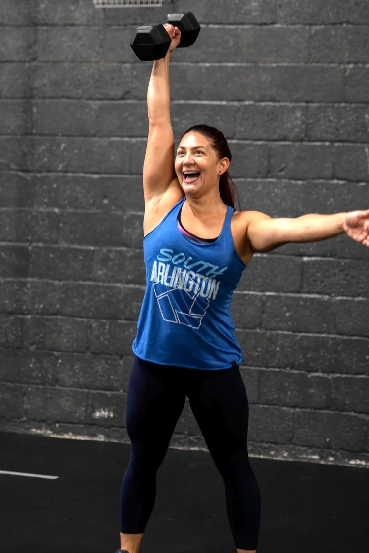 A woman laughs as she presses a dumbbell overhead
