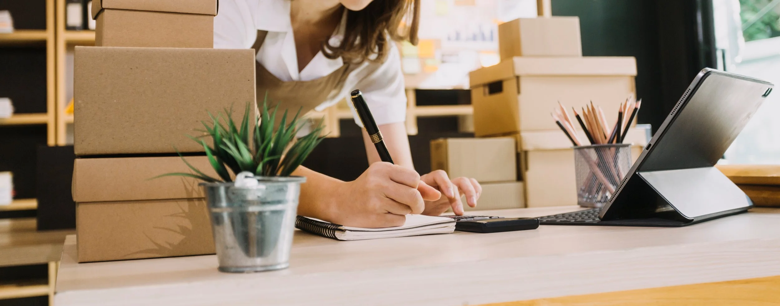 woman leaning over desk writing order with boxes surrounding.jpeg
