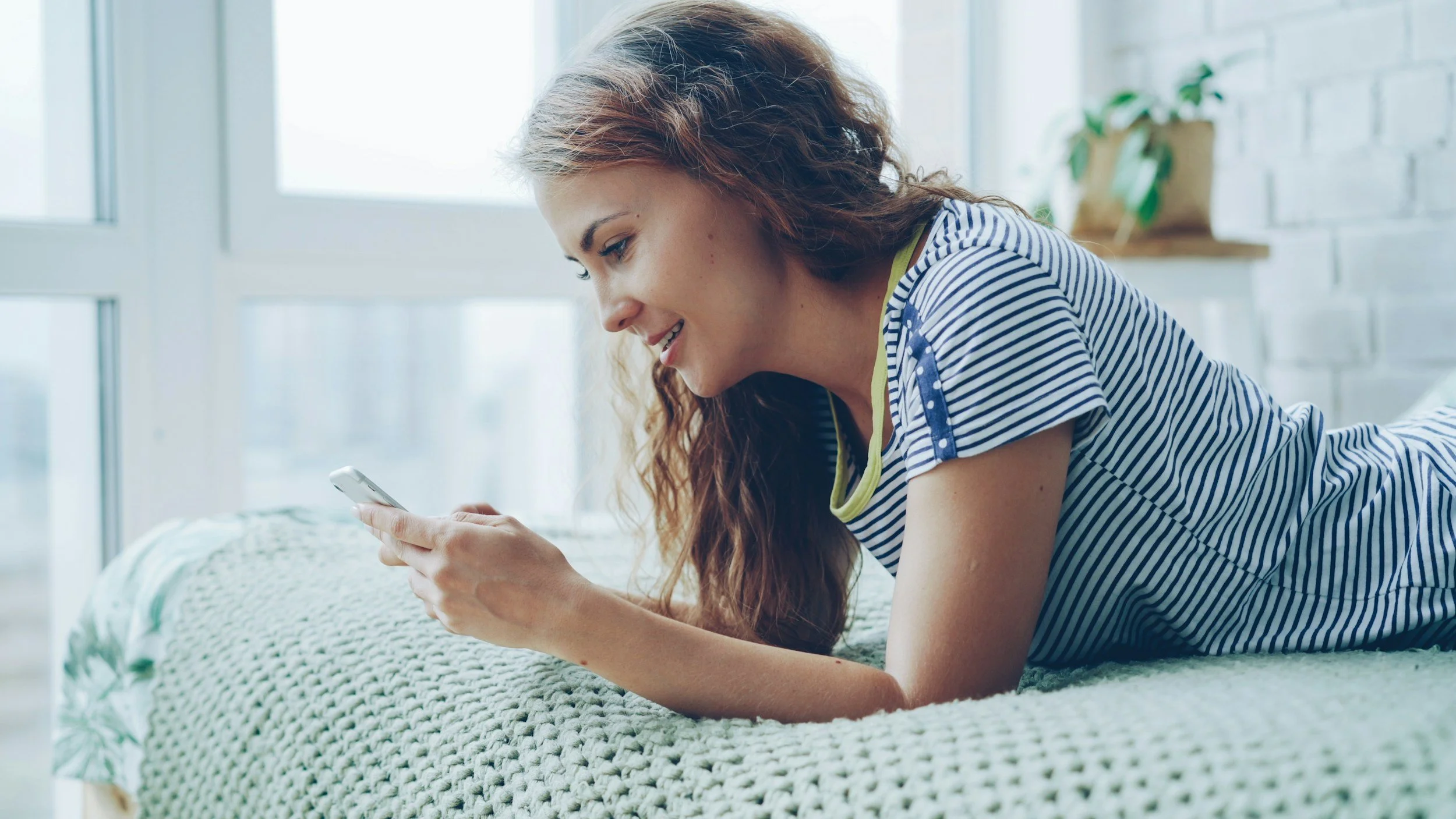 Teenage girl, lying on her bed in a bright room looking at her phone.