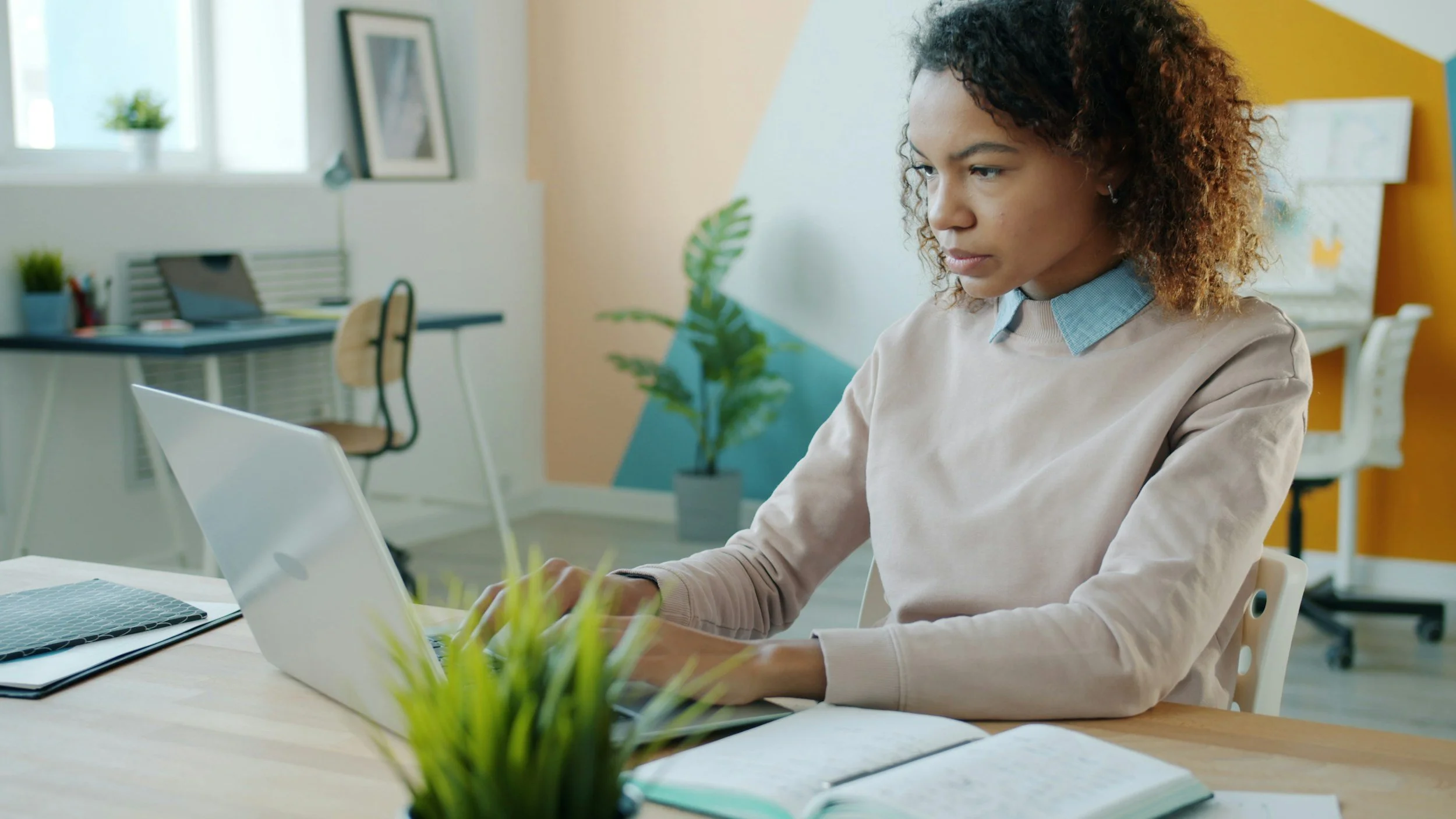 Administrative professional working at a laptop in a bright office with a notebook on the desk.